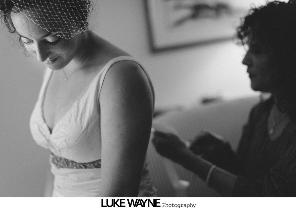 Bride in a wedding dress, with a woman assisting with the back of the dress.