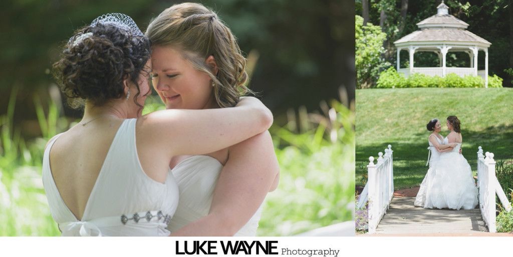 Two brides in white dresses embracing, smiling, outdoors.