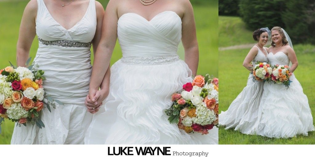 Two brides holding hands, each in a white wedding dress, holding bouquets of flowers on a grassy lawn.