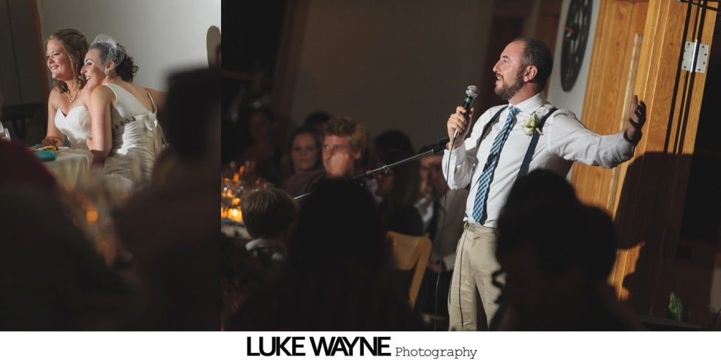 Man giving a speech at a wedding, brides seated at table.