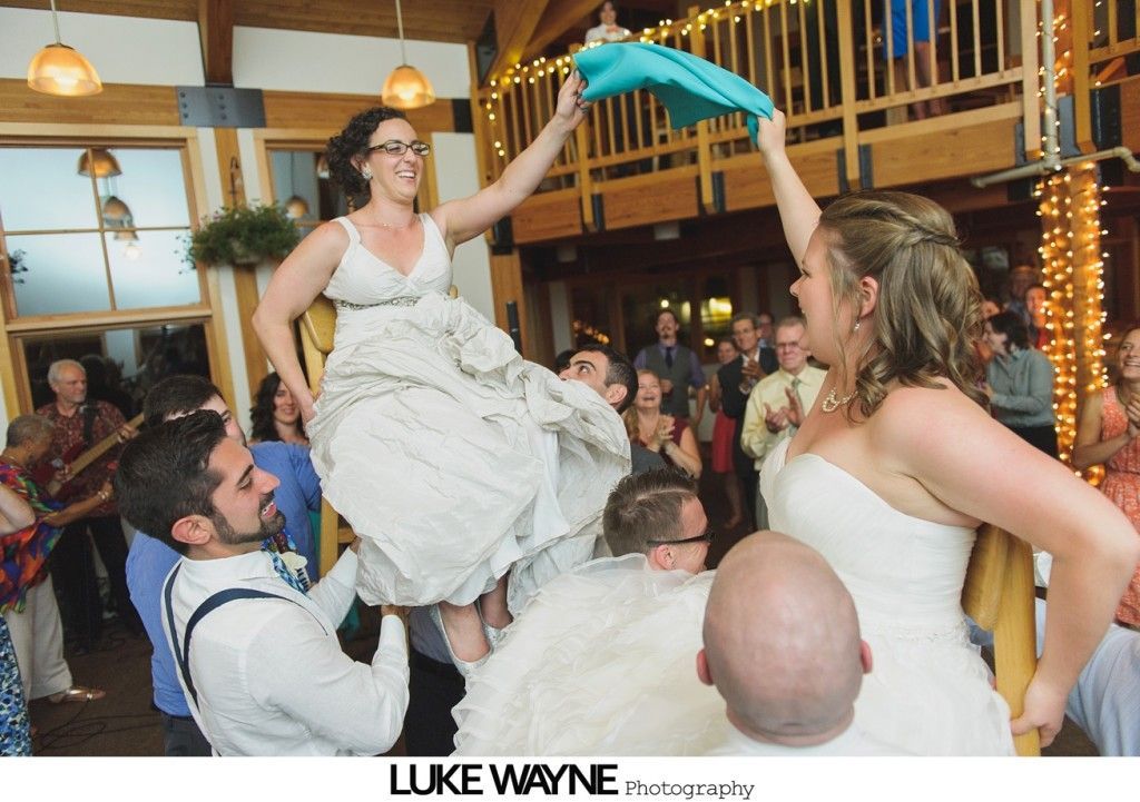 Two brides being lifted at a wedding reception, one holding a blue cloth.