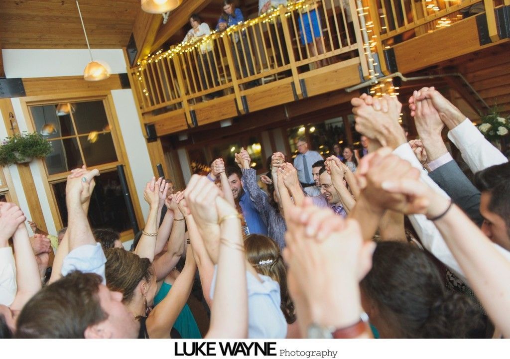 People holding hands up, lit from below, in a wood-paneled room with a balcony.