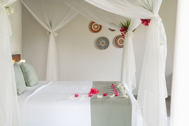 Quarto com cama de dossel branca, detalhes em verde claro e arte decorativa na parede.