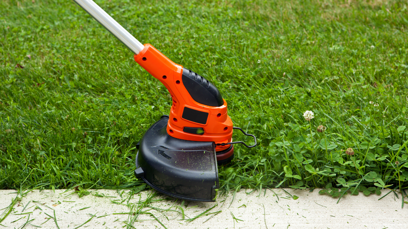 Orange string trimmer cutting grass along a concrete edge on a lawn