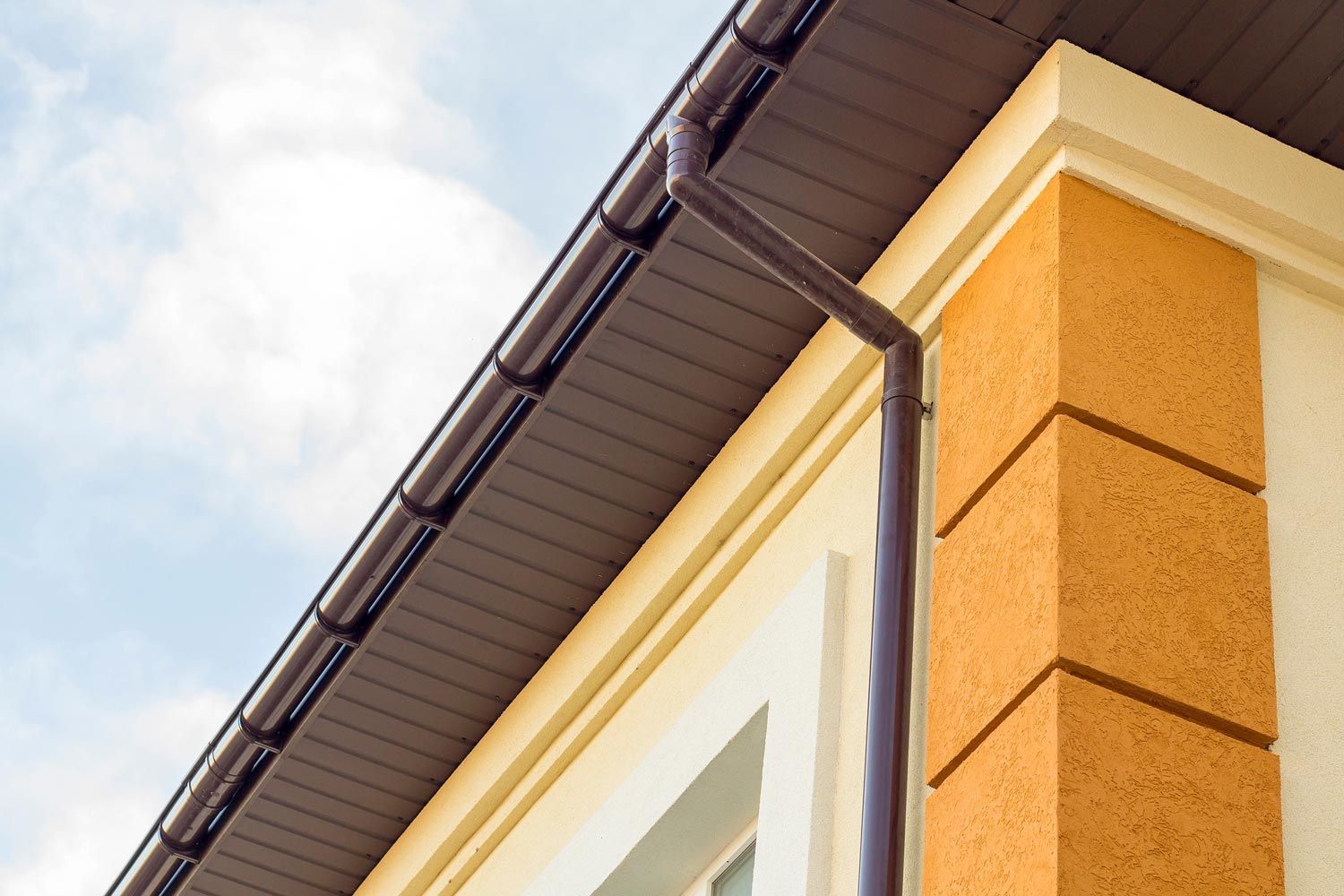 Corner of a house with orange stucco walls, white trim, and dark roof gutters against a cloudy sky Corner of a house with orange stucco walls, white trim, and dark roof gutters against a cloudy sky