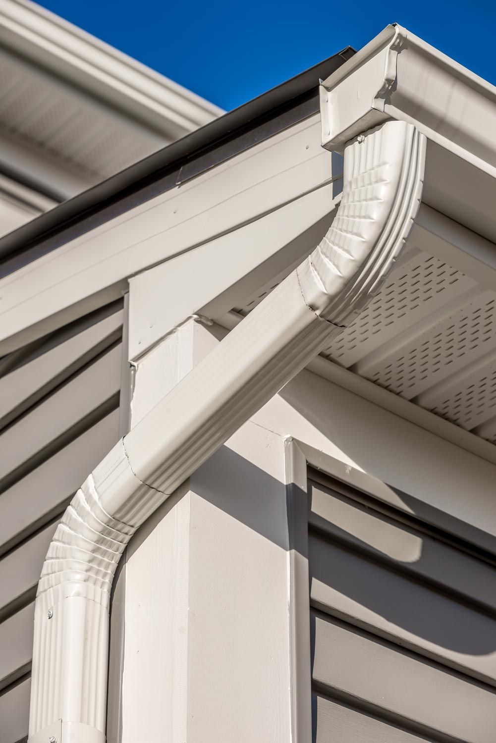 White rain gutter and downspout on a house roof corner against blue sky White rain gutter and downspout on a house roof corner against blue sky
