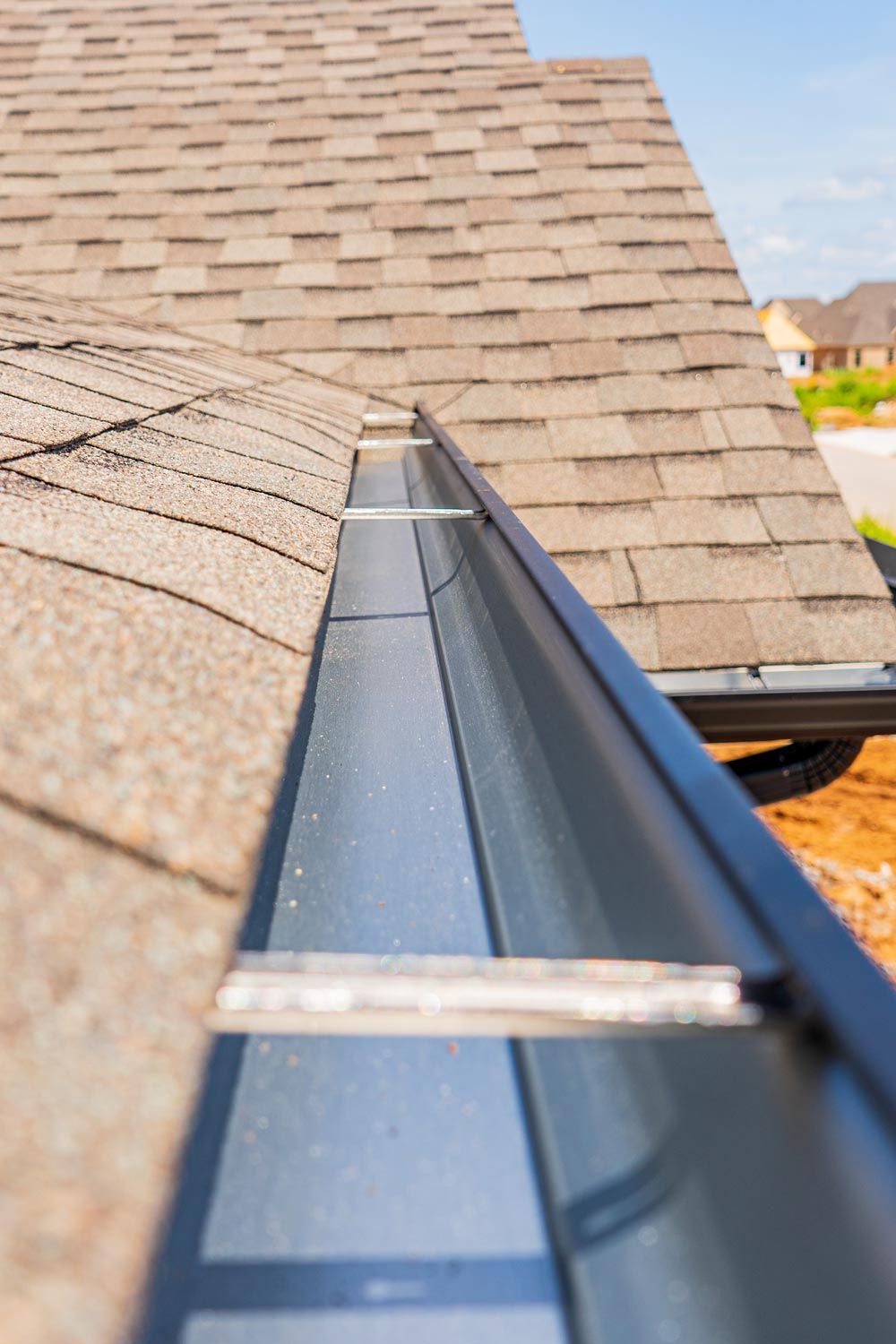 Gutter installed along shingled roof eave, showing close-up of black metal channel. Gutter installed along shingled roof eave, showing close-up of black metal channel.