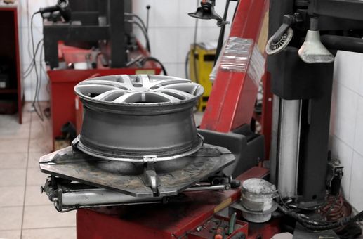 A car wheel on a tire machine in an auto shop. Red, silver, black, and gray.