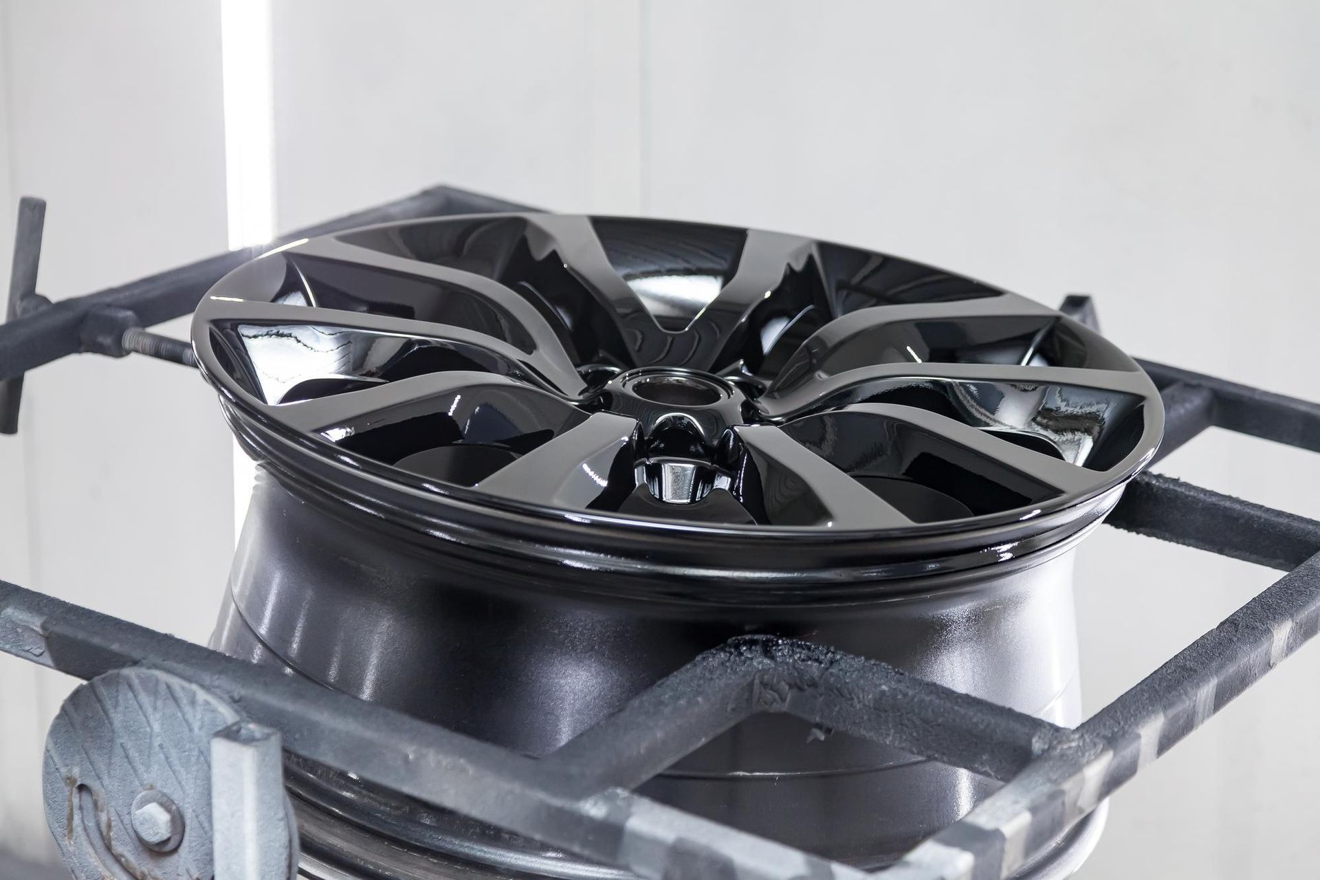 Black car wheel in the process of being painted, mounted on a stand inside a paint booth.