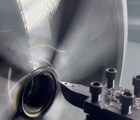 A lathe machine cutting metal, producing shiny swarf. Tool is mounted, rotating metal piece.
