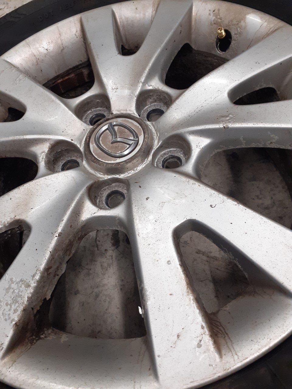 Silver Mazda car wheel with center logo and bolt holes.