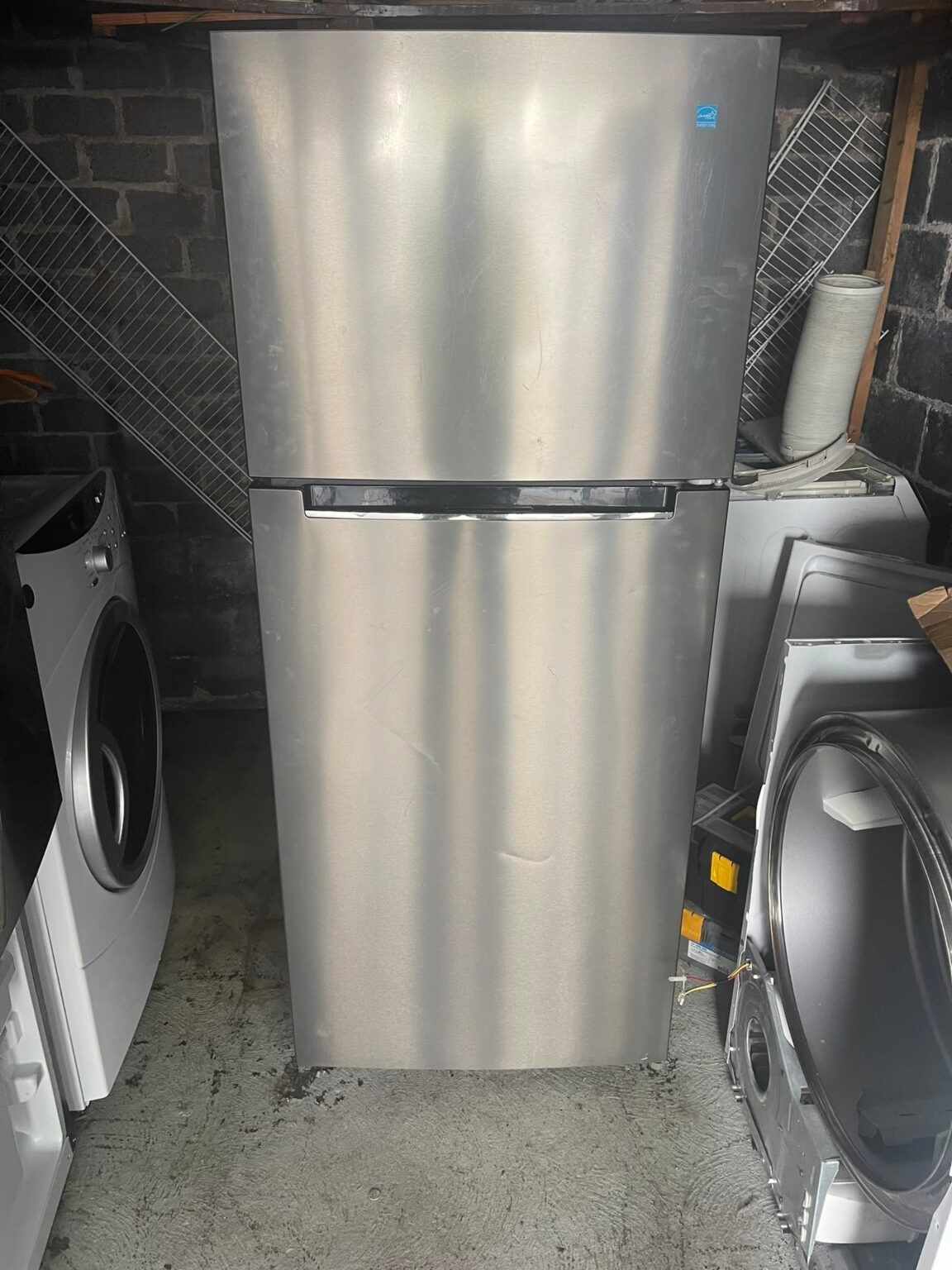 A stainless steel refrigerator is sitting in a garage next to a washer and dryer.