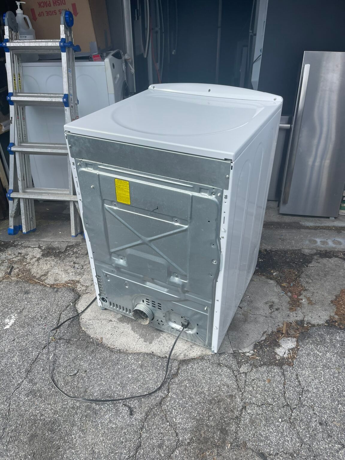 A white dryer is sitting on the side of the road next to a ladder.