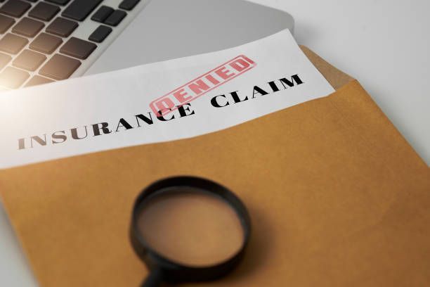 A magnifying glass is sitting on top of an envelope with a denied insurance claim on it.