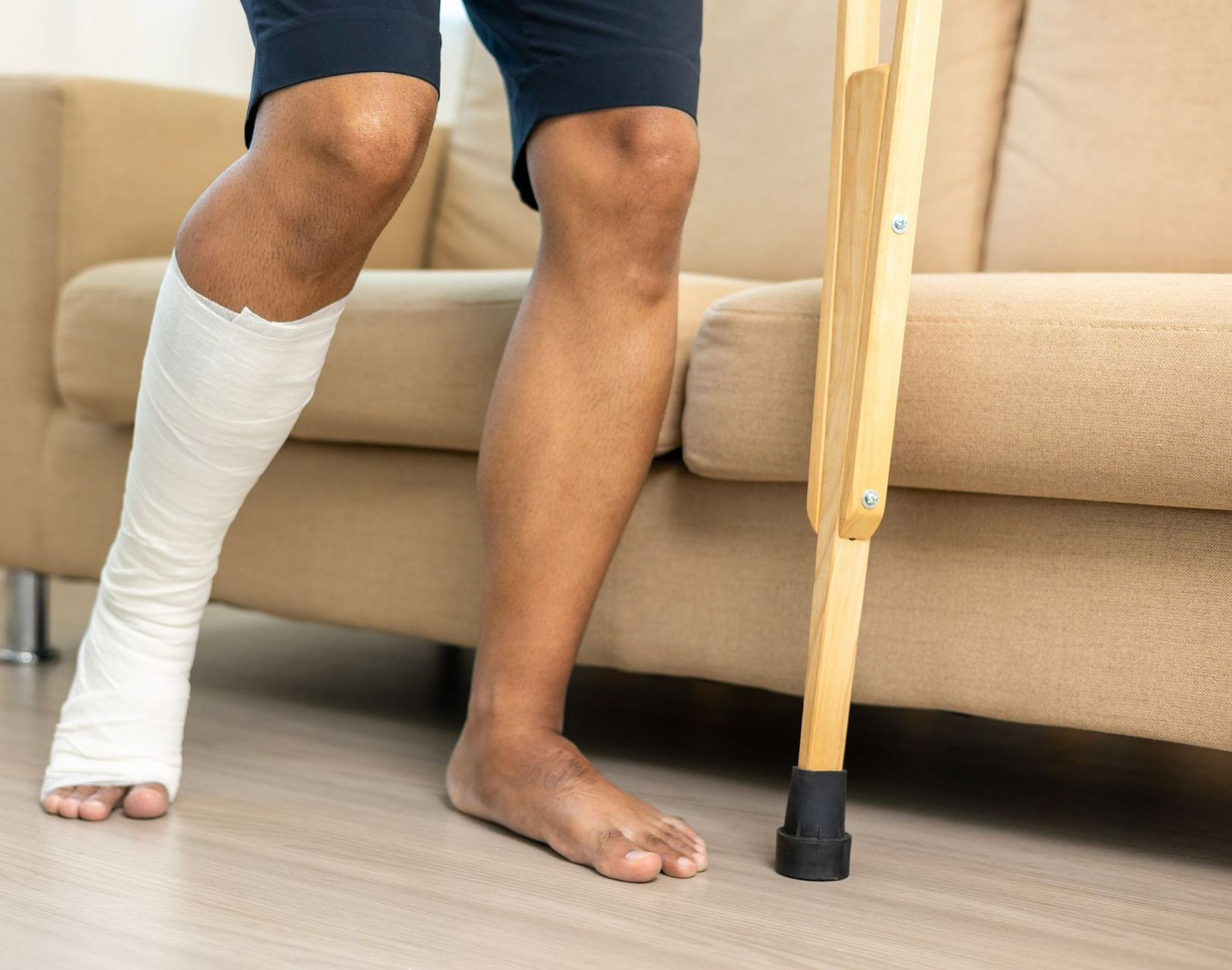 A man with a cast on his leg is standing next to a couch with crutches.