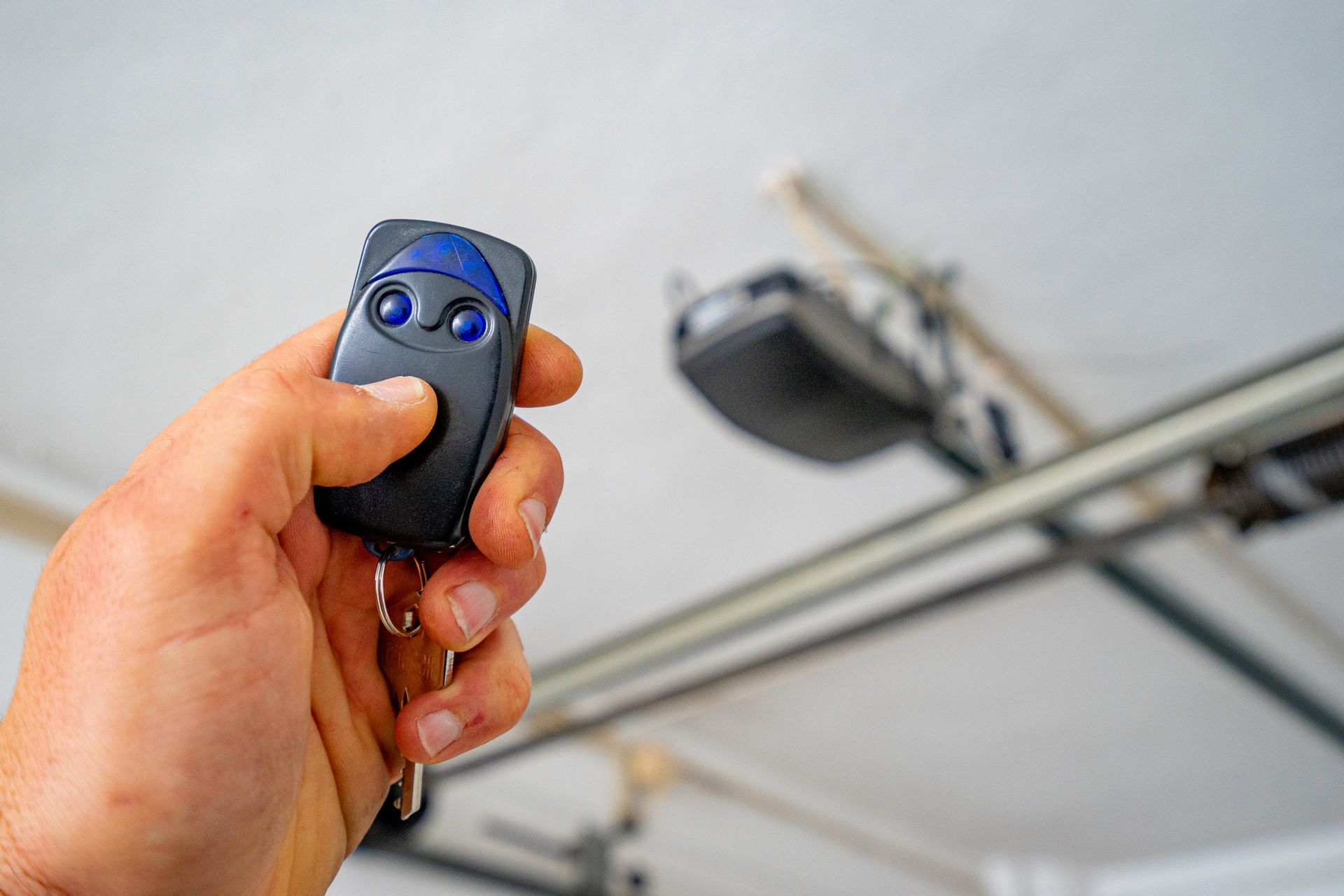 Hand holding a garage door opener, pressing the button near the mounted opener unit.