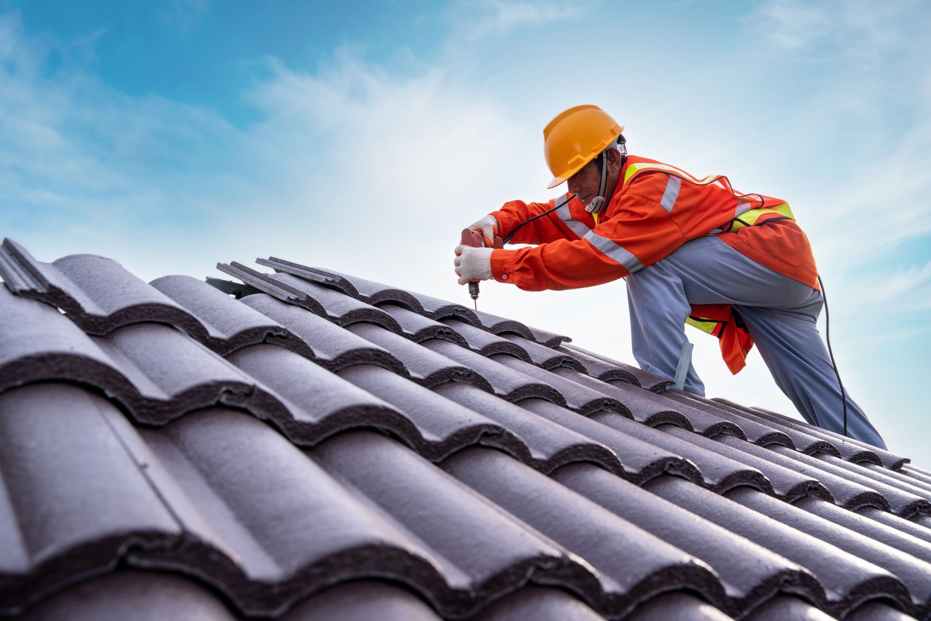 A roofing contractor working on a rooftop, equipped with safety gear, is installing a roof.