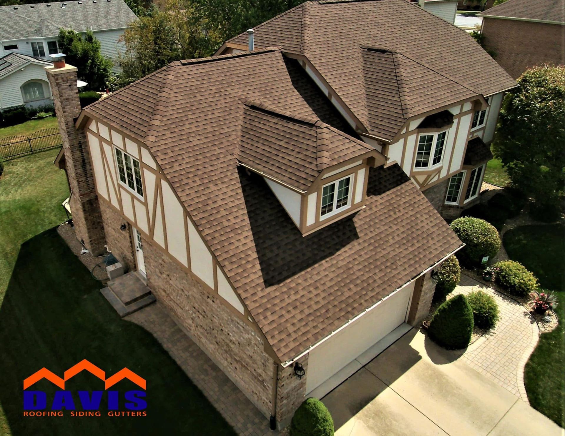 Brown shingled roof on a two-story house with tan and brown exterior, chimney, and dormer.