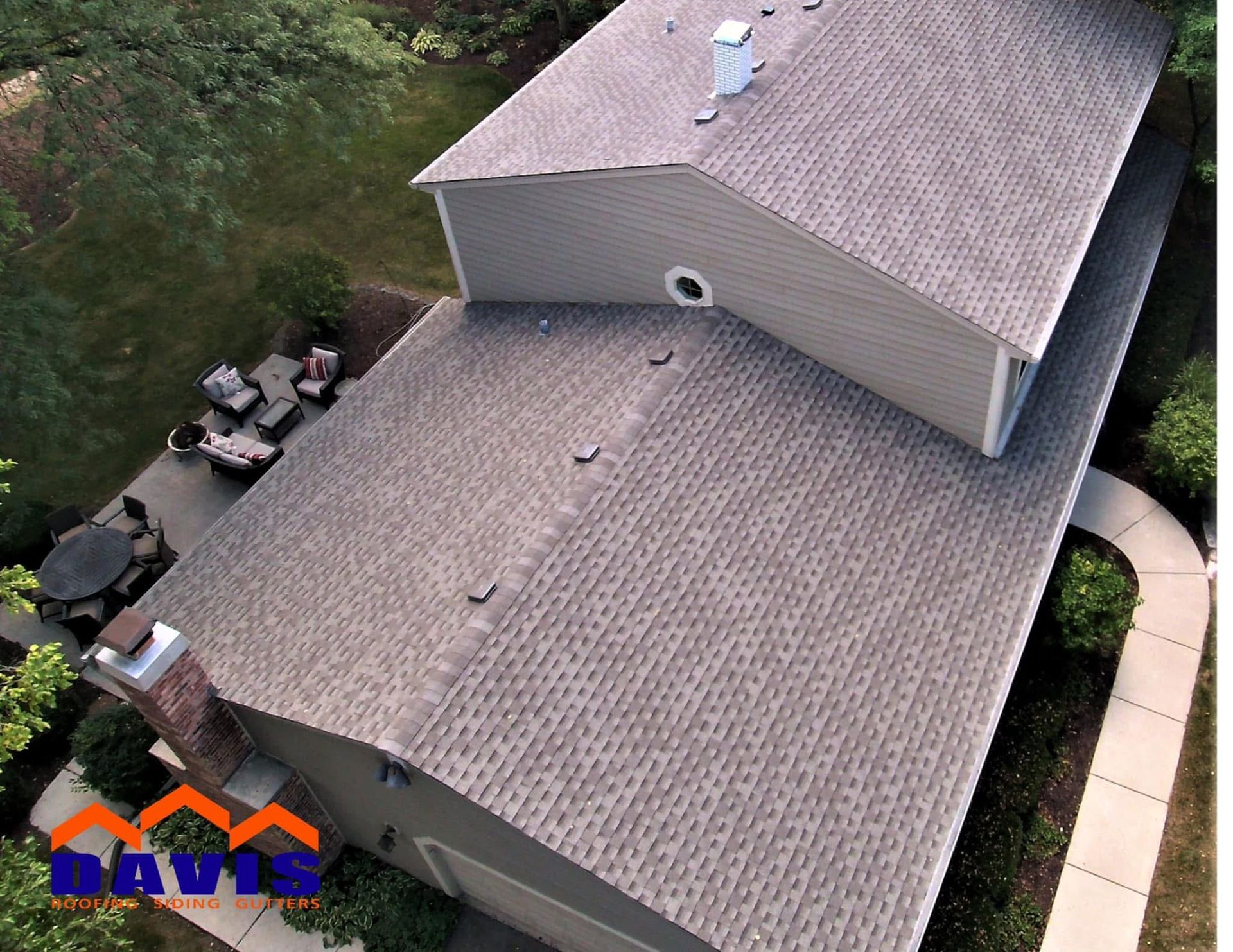 Overhead view of a house with a brown shingle roof, chimney, and patio with seating.