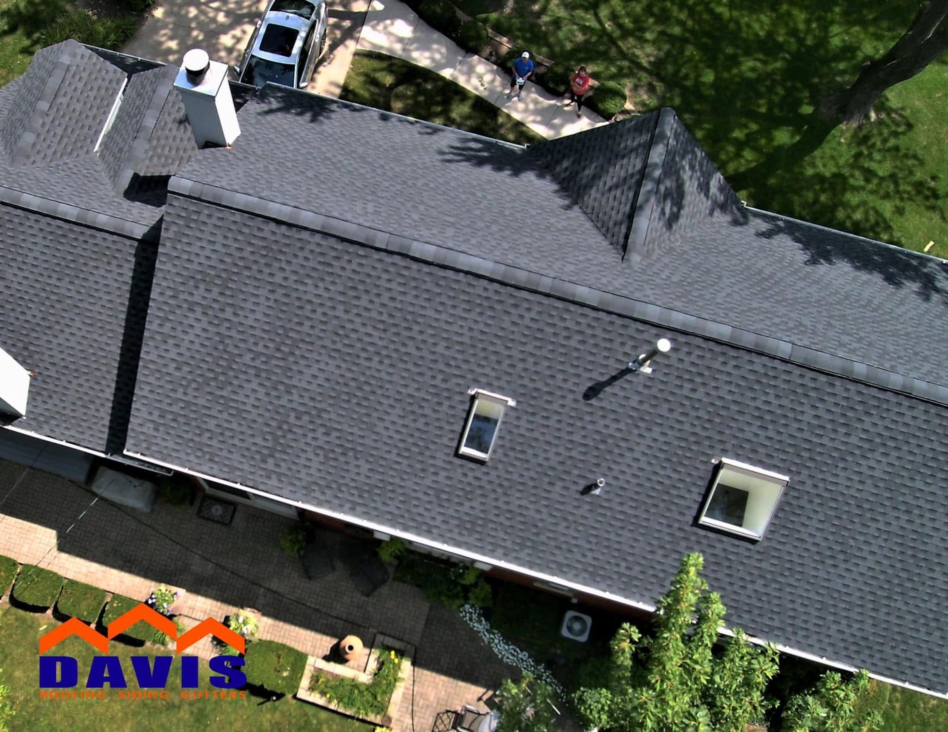 Aerial view of a dark gray shingle roof with skylights and a chimney.