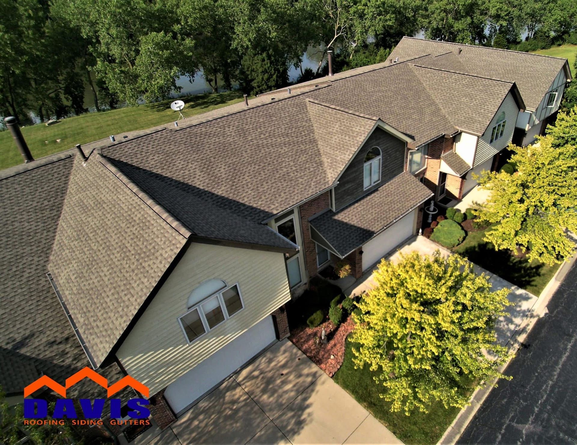 Aerial view of townhouses with gray shingle roofs, surrounded by trees and a paved driveway.