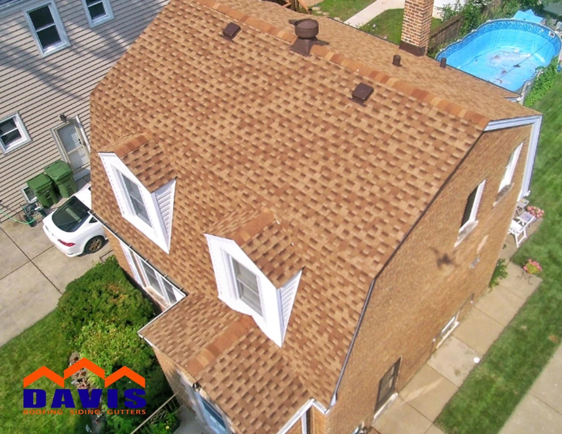 Brown roof on a two-story brick house with white window frames. A pool is in the backyard.