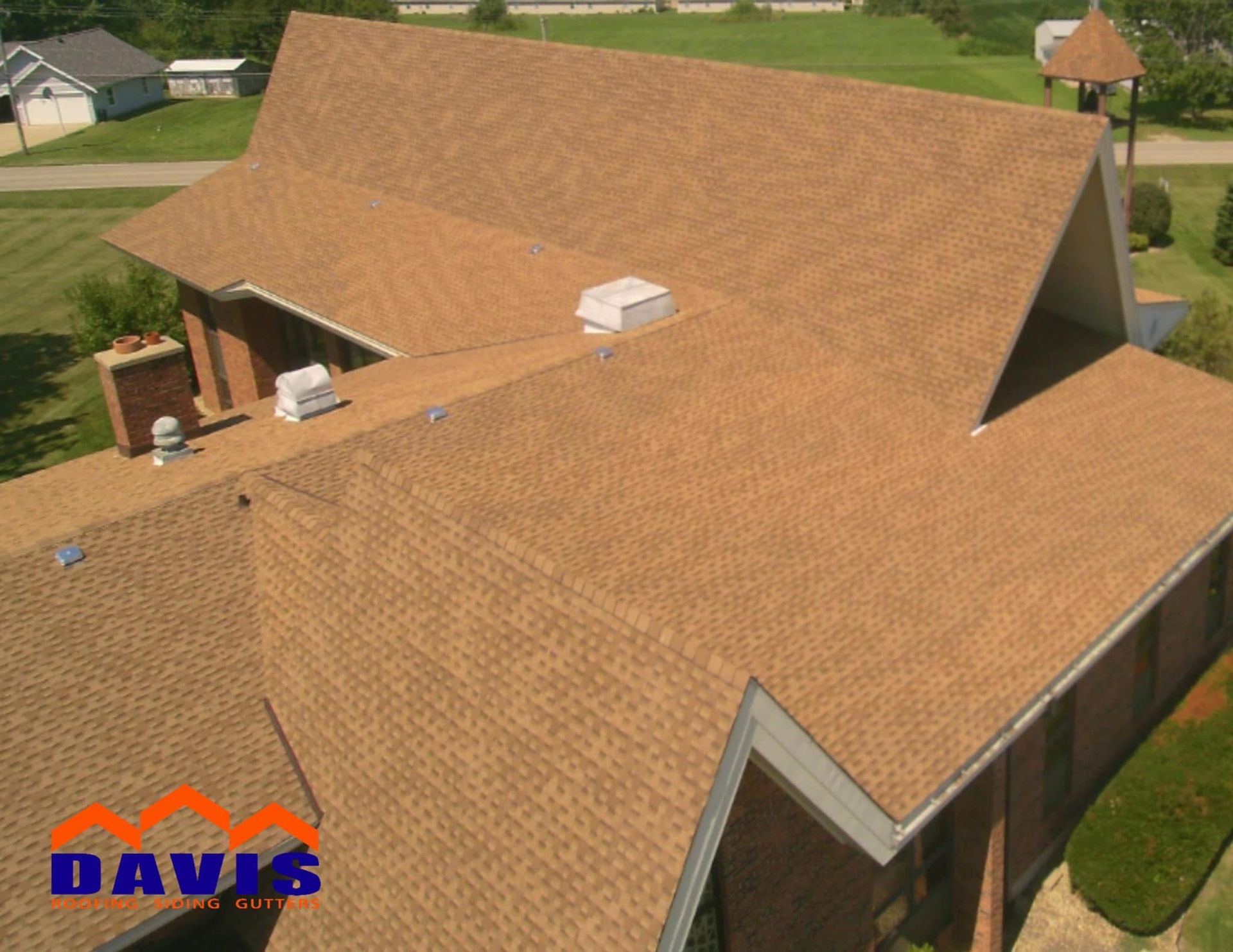 Brown shingle roof of a building with several roof sections and a brick chimney.