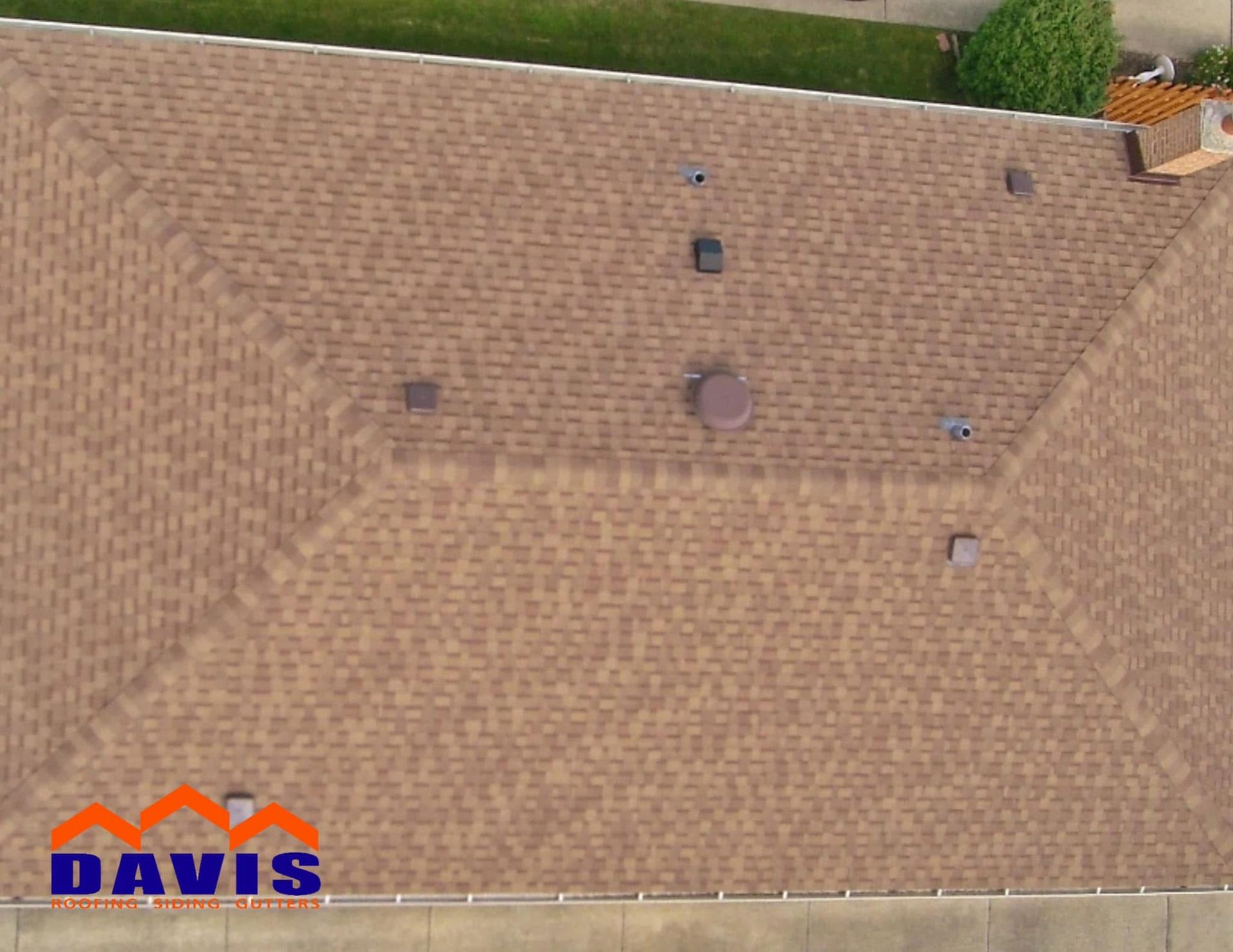 Brown shingled roof of a house with several vents and a chimney. Aerial view.