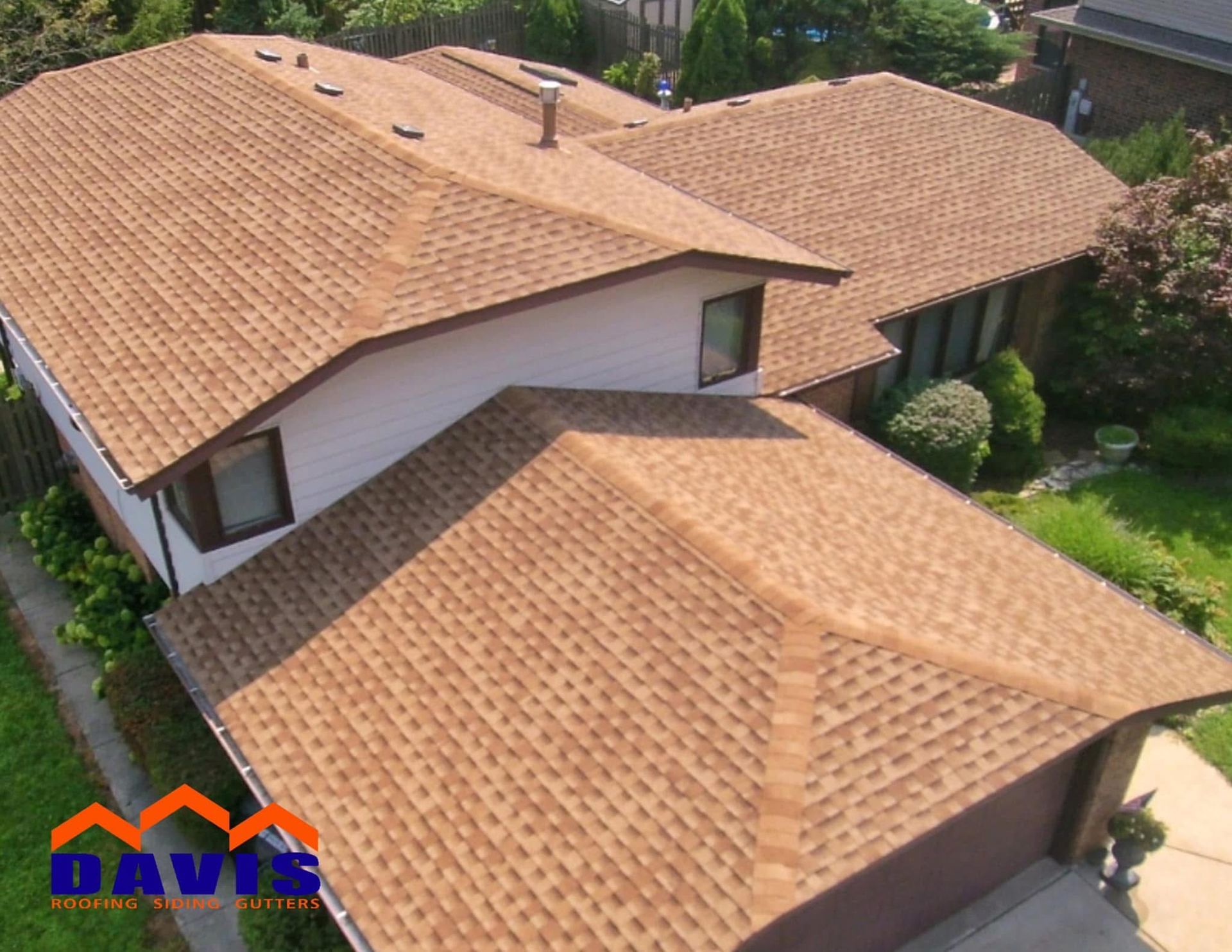 Brown asphalt shingle roof on a residential house with green lawn.