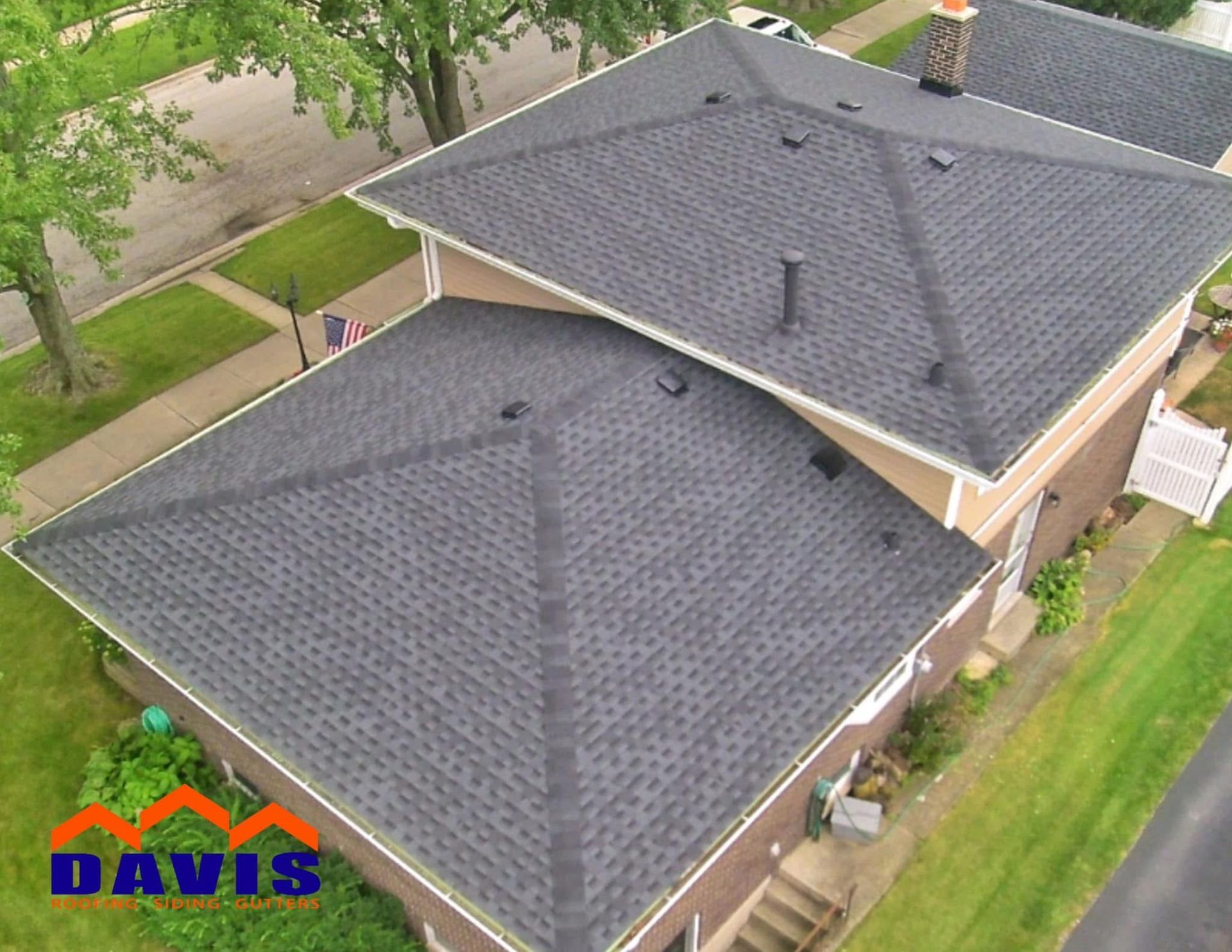 Aerial view of a home with a newly installed dark gray shingle roof. Green grass and trees surround the house.