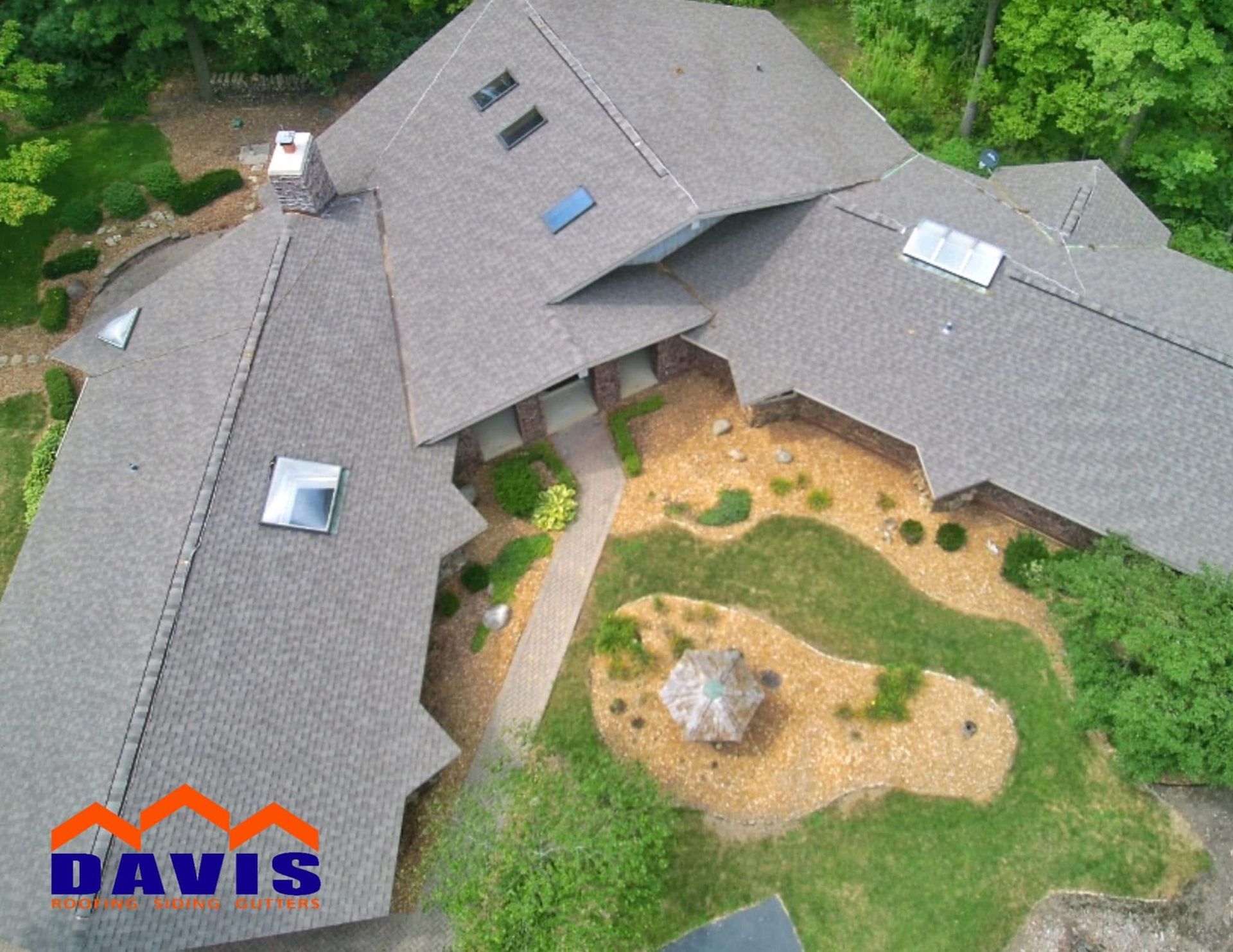 Aerial view of a home with a complex, multi-level roof. Gray shingles, landscaping, and a walkway are visible.