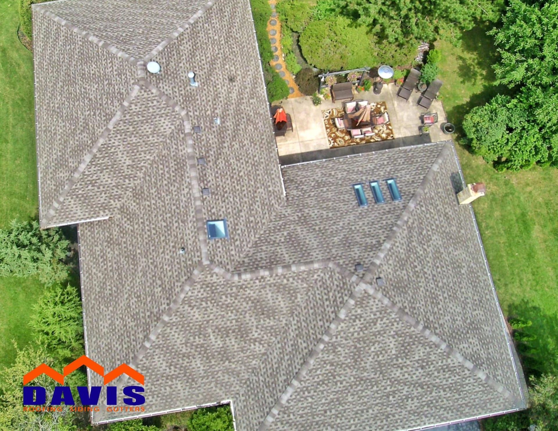 Aerial view of a gray roof with vents and skylights, next to a patio and green lawn.