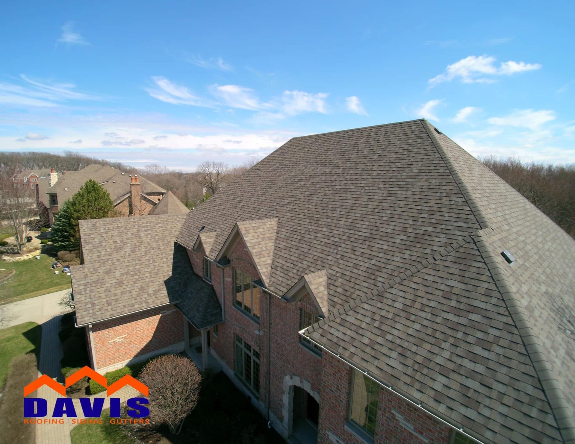 Aerial view of a brown shingled roof on a brick home with blue sky, and a Davis logo.