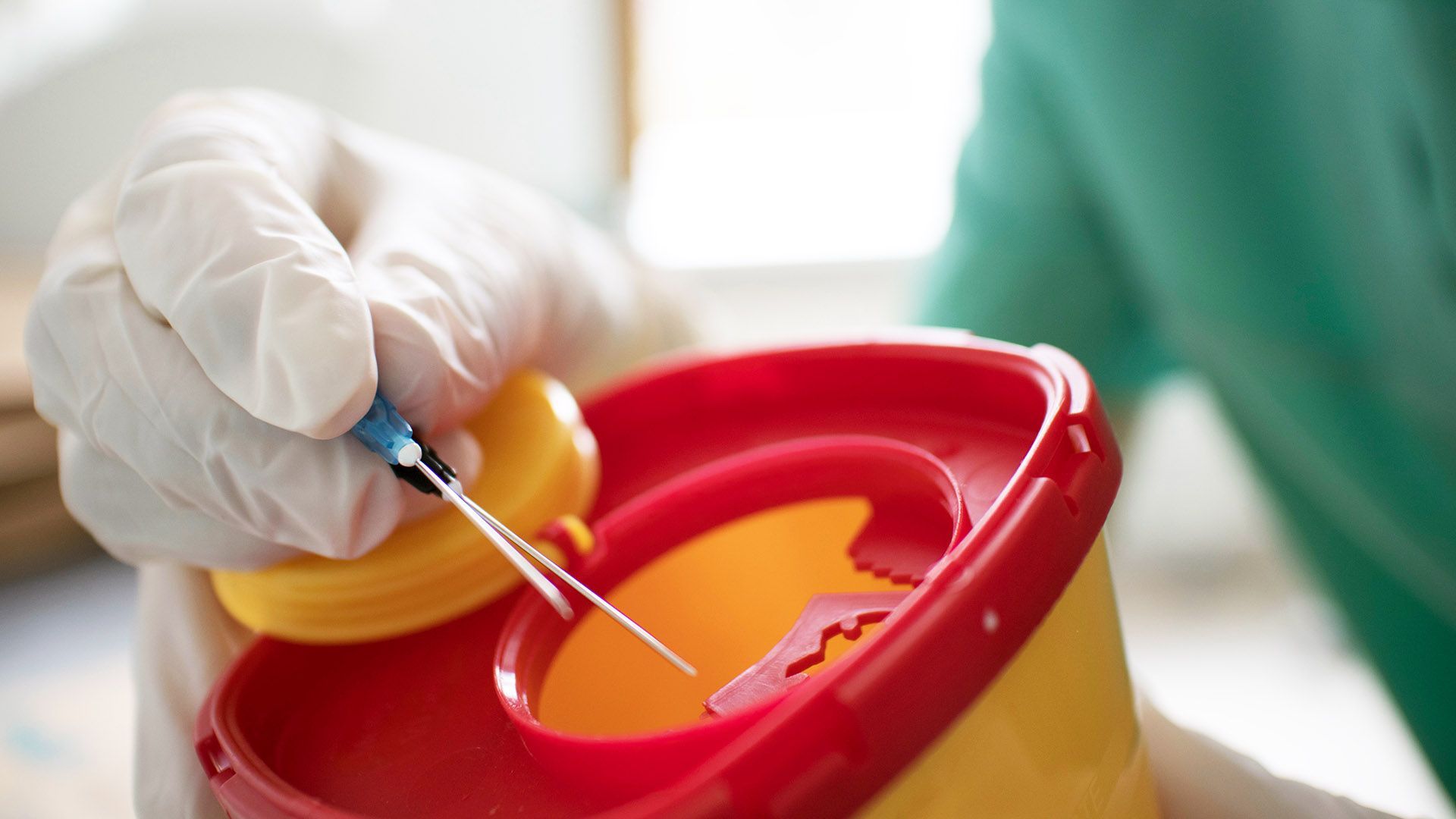 A person wearing blue gloves is putting a needle in a sharps bin.