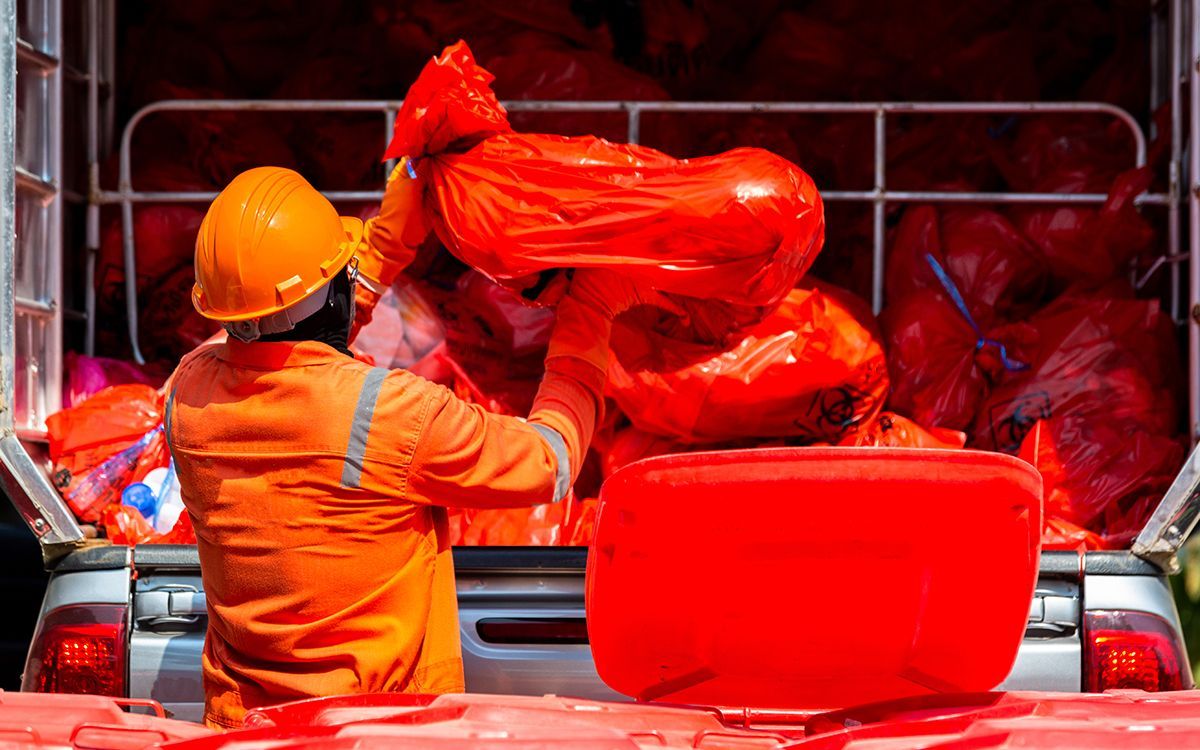 A medical disposal worker putting red trash bags full of medical waste into a disposal truck 