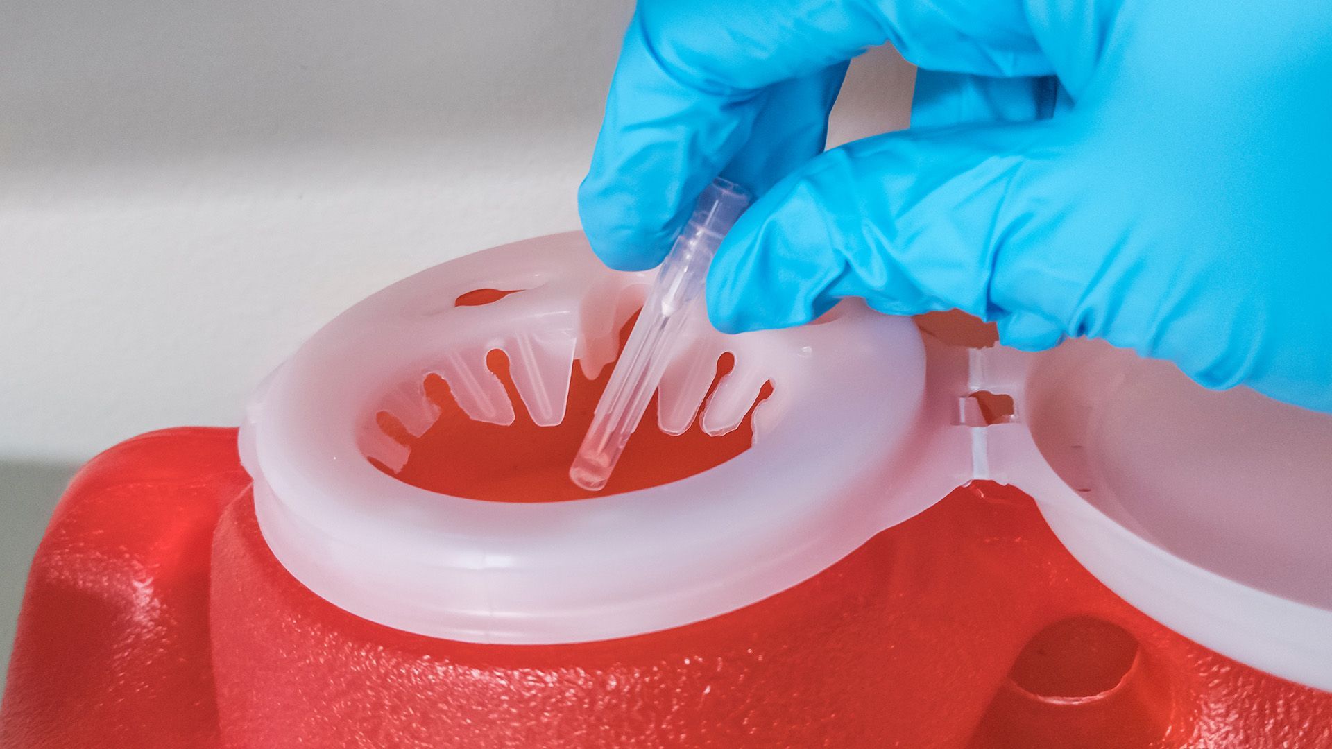 A person wearing blue gloves is putting a needle in a sharps bin.
