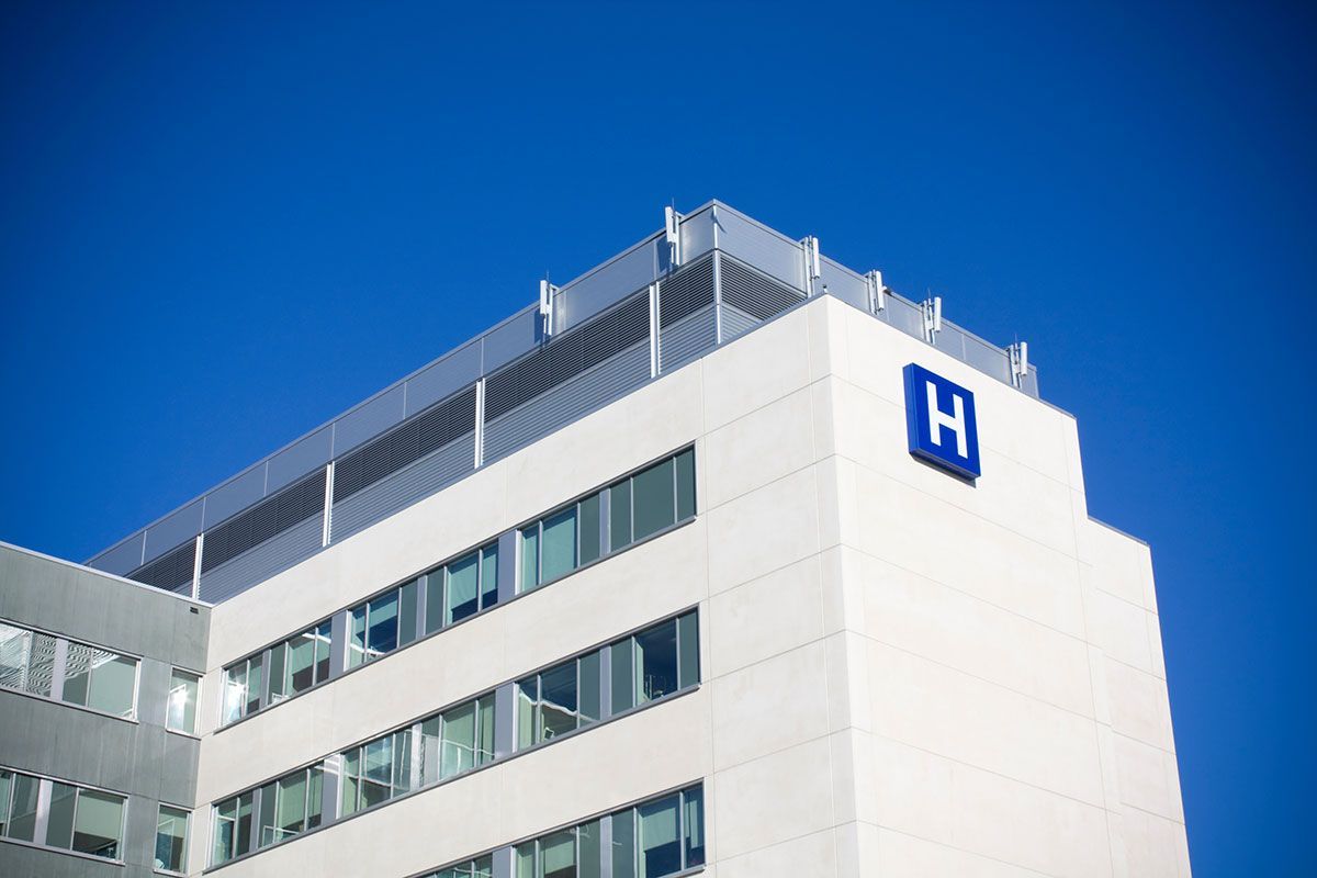Modern white hospital building with blue signage against a clear blue sky