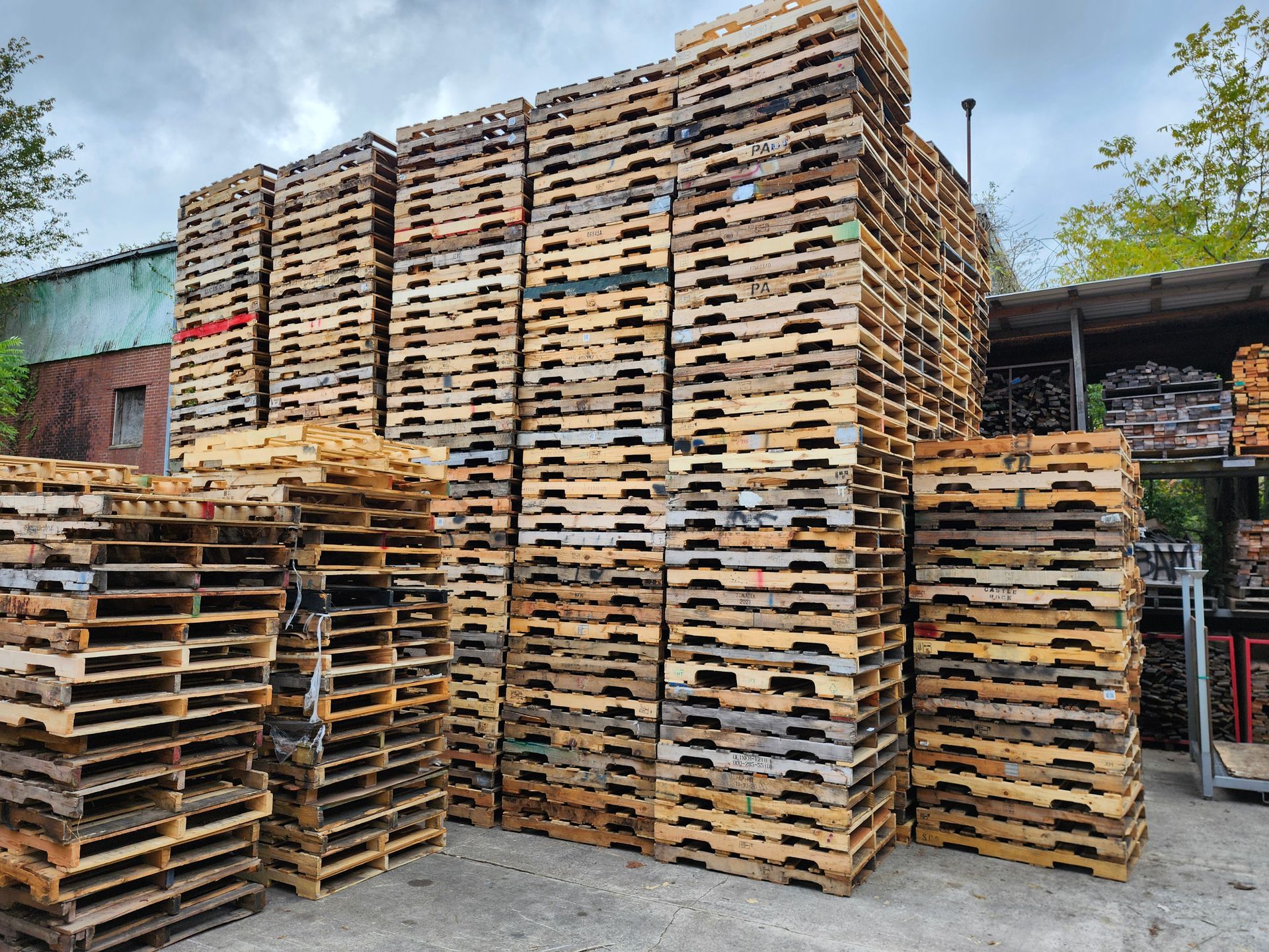 Stacks of wooden pallets outdoors, brown and weathered, against a building.
