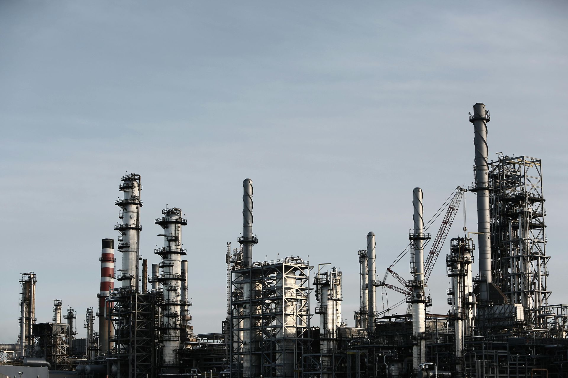Oil refinery with many towers and chimneys against a hazy sky.