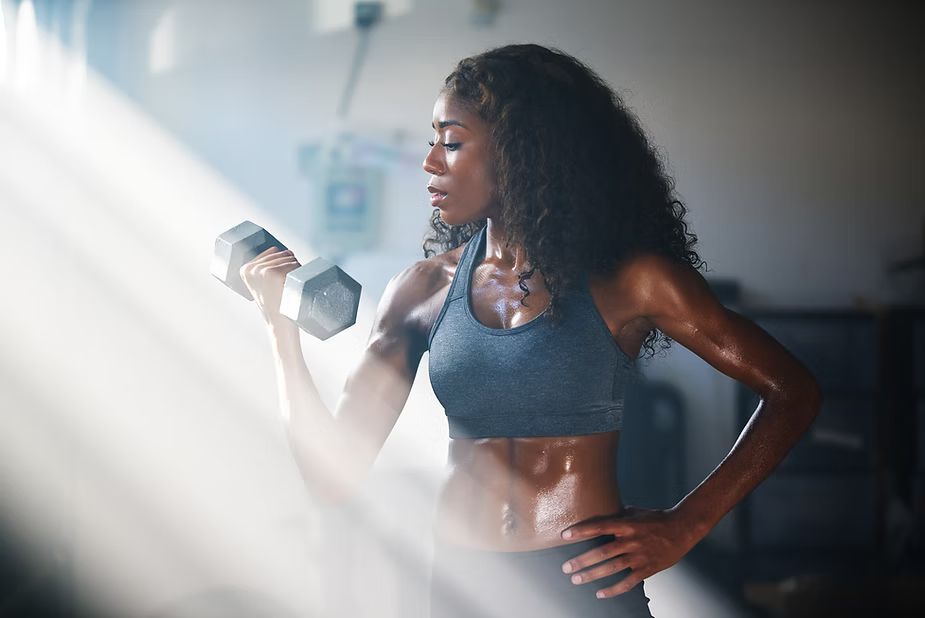 Woman lifting dumbbell, sweaty, in a dimly lit gym, focused expression.
