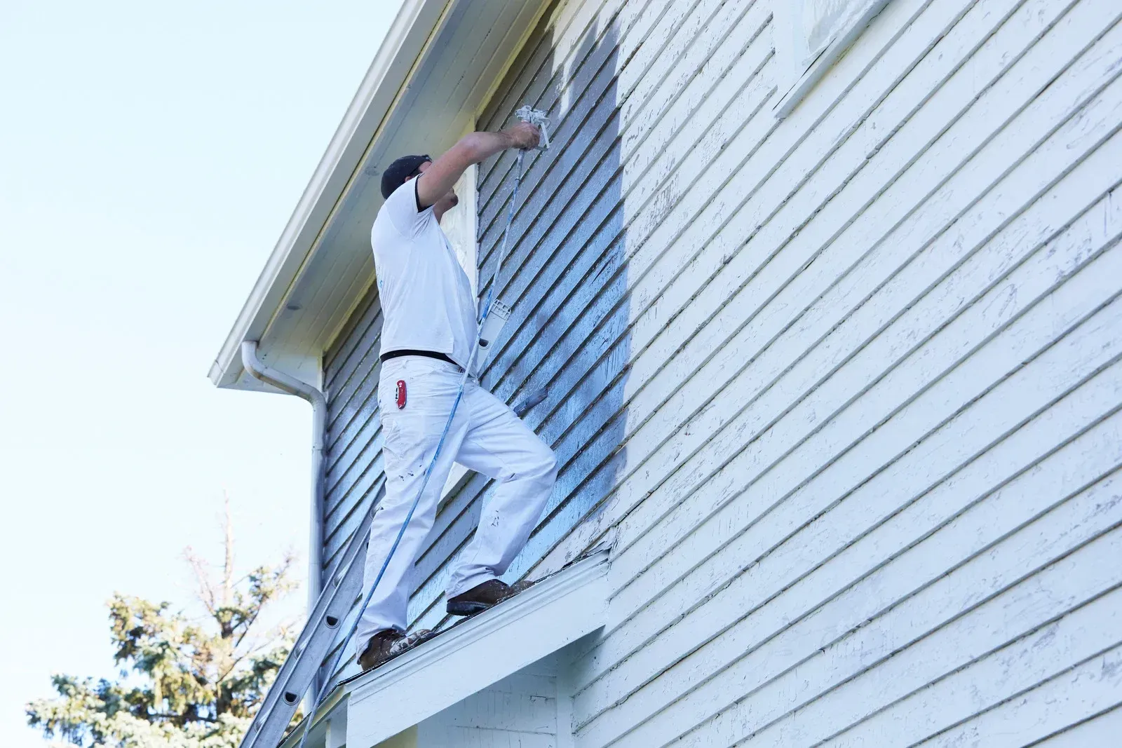 A man is standing on a ladder painting the side of a house.