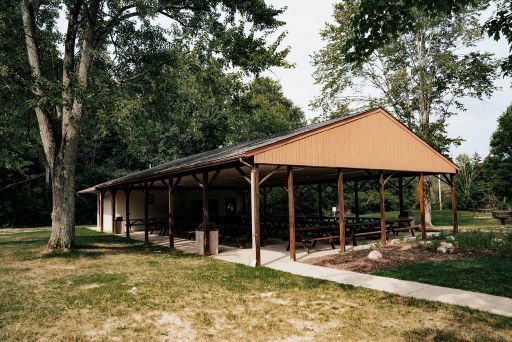 A pavilion with tables and benches in a park with trees in the background.