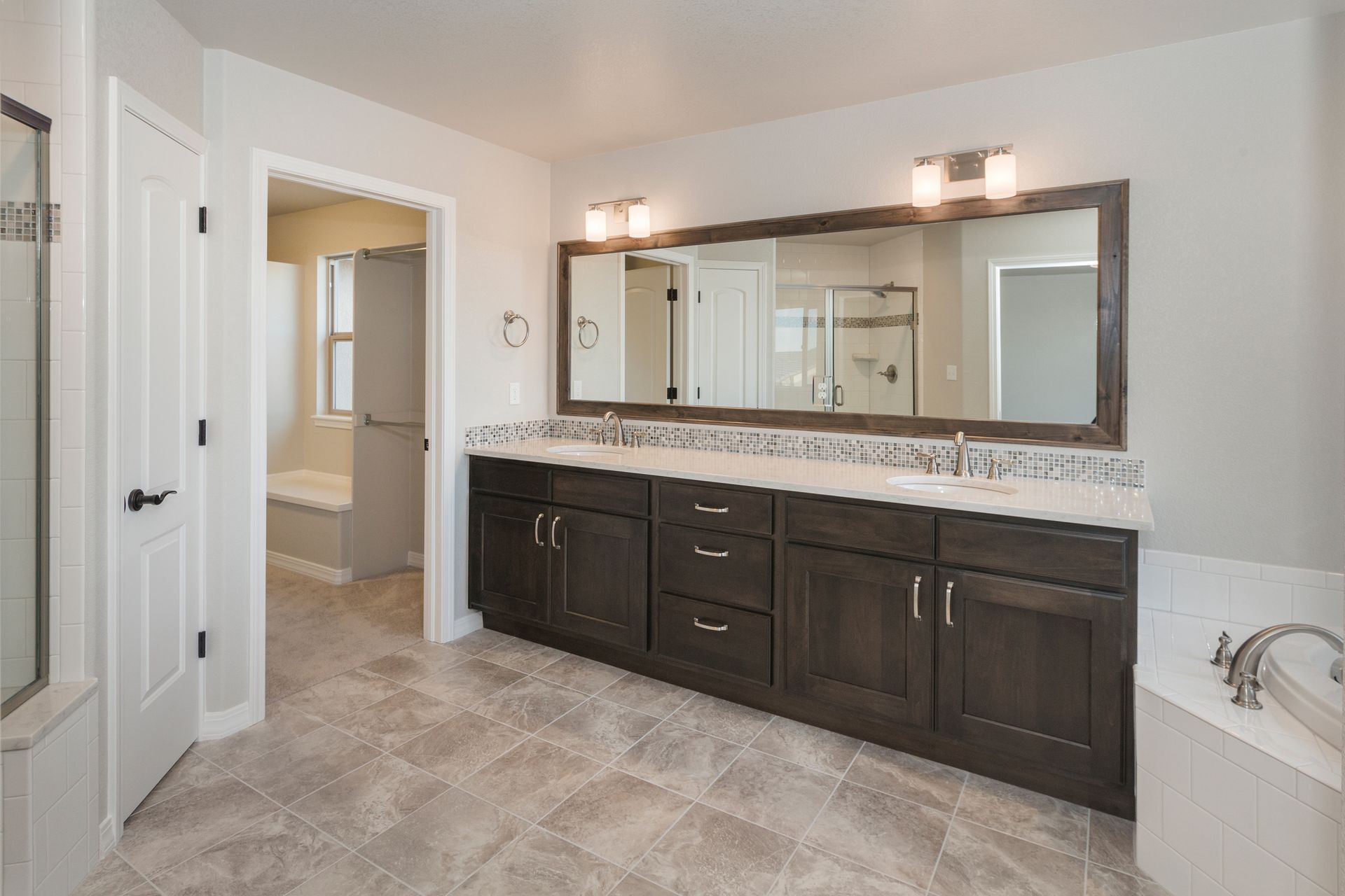 Spacious master bathroom with dark wood vanity, large mirror, and neutral-toned tile flooring.