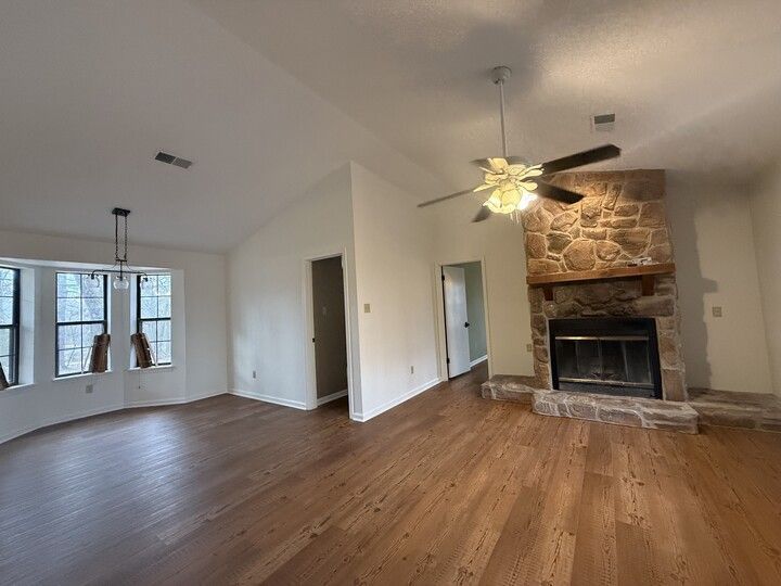 Living room with stone fireplace, wooden floors, and white walls.