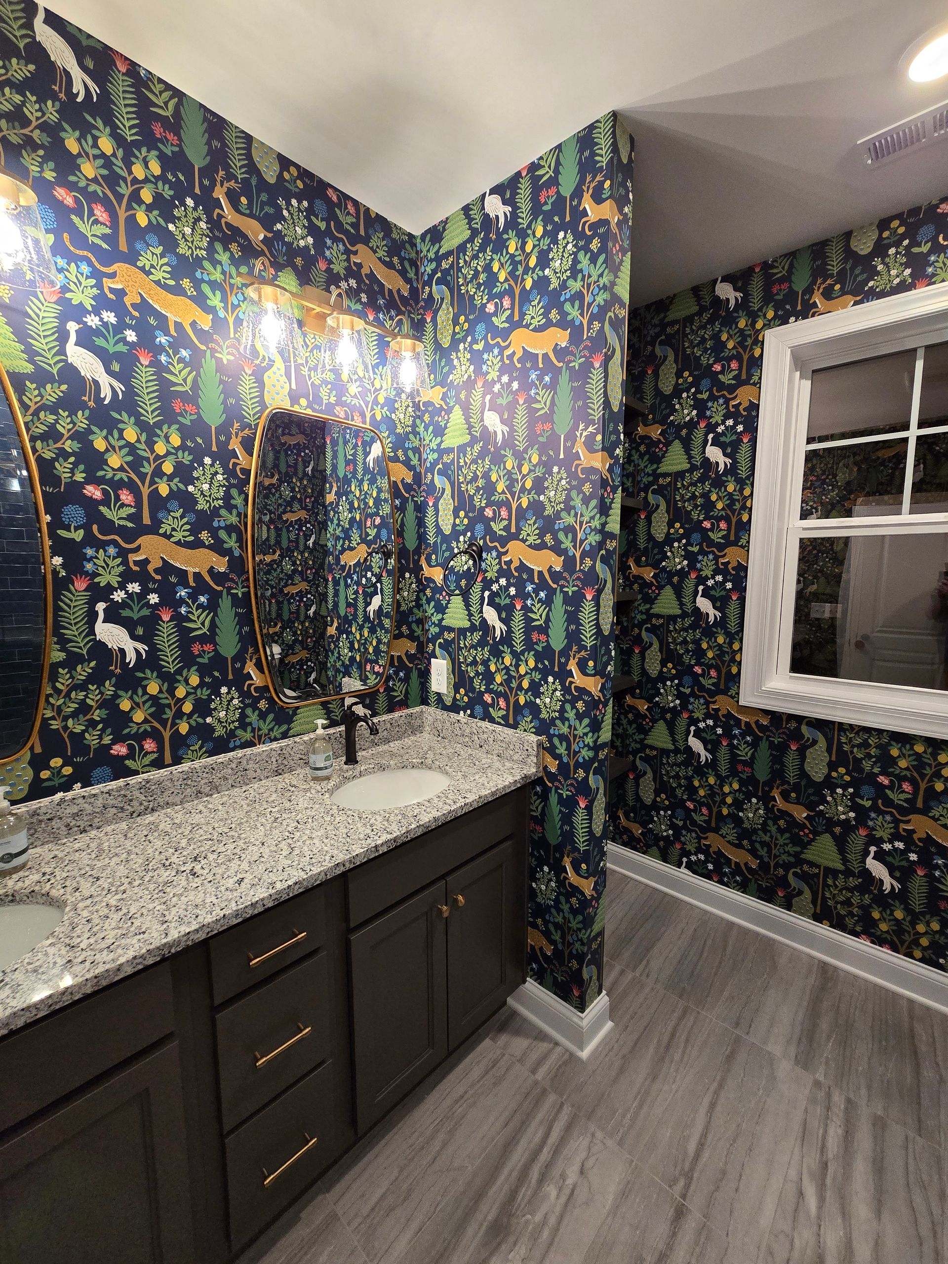 Bathroom with dark blue wallpaper featuring forest animals, dark cabinets, and a granite countertop.