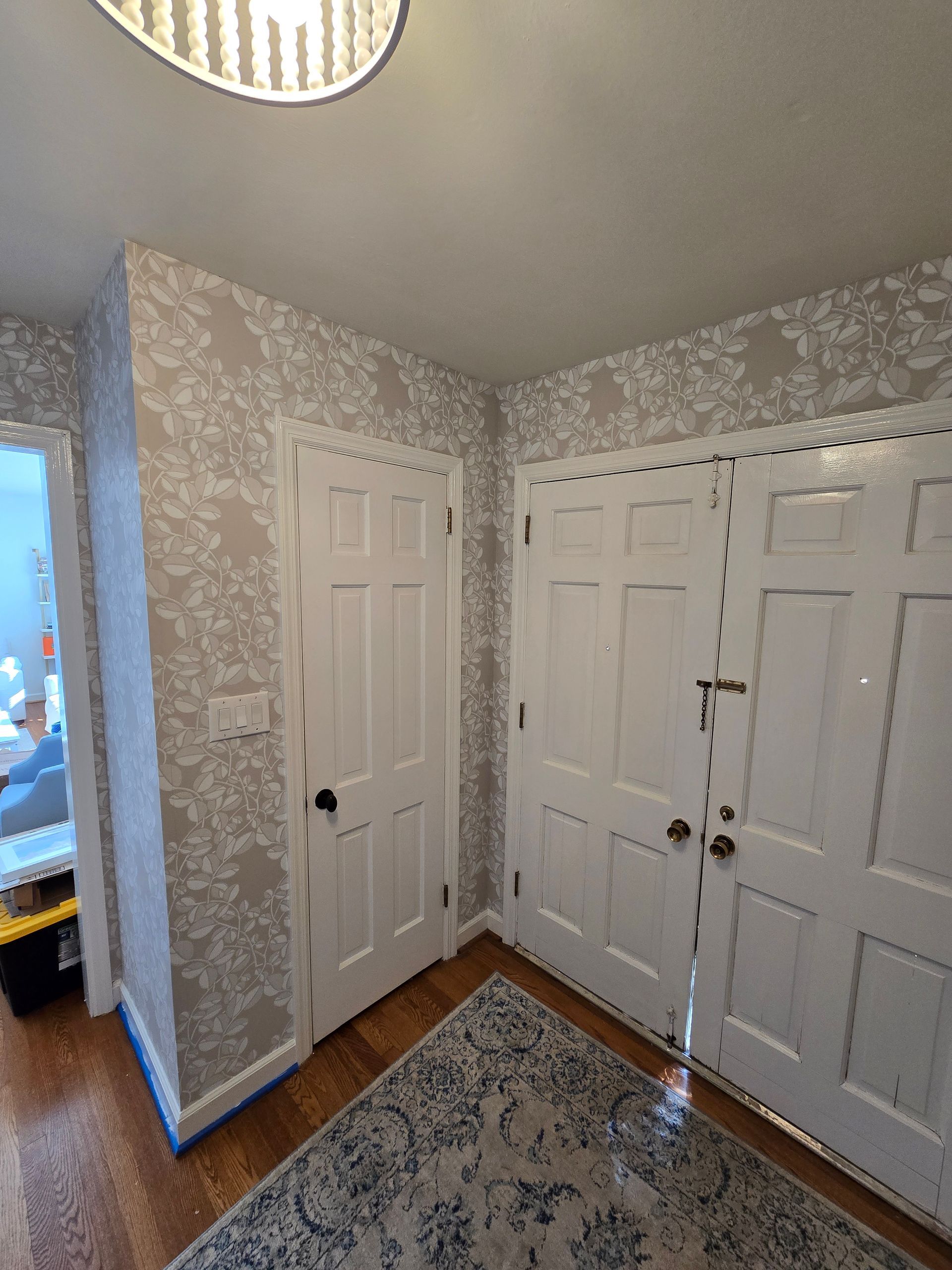 Hallway with floral wallpaper, white doors, and a patterned rug on a wooden floor.