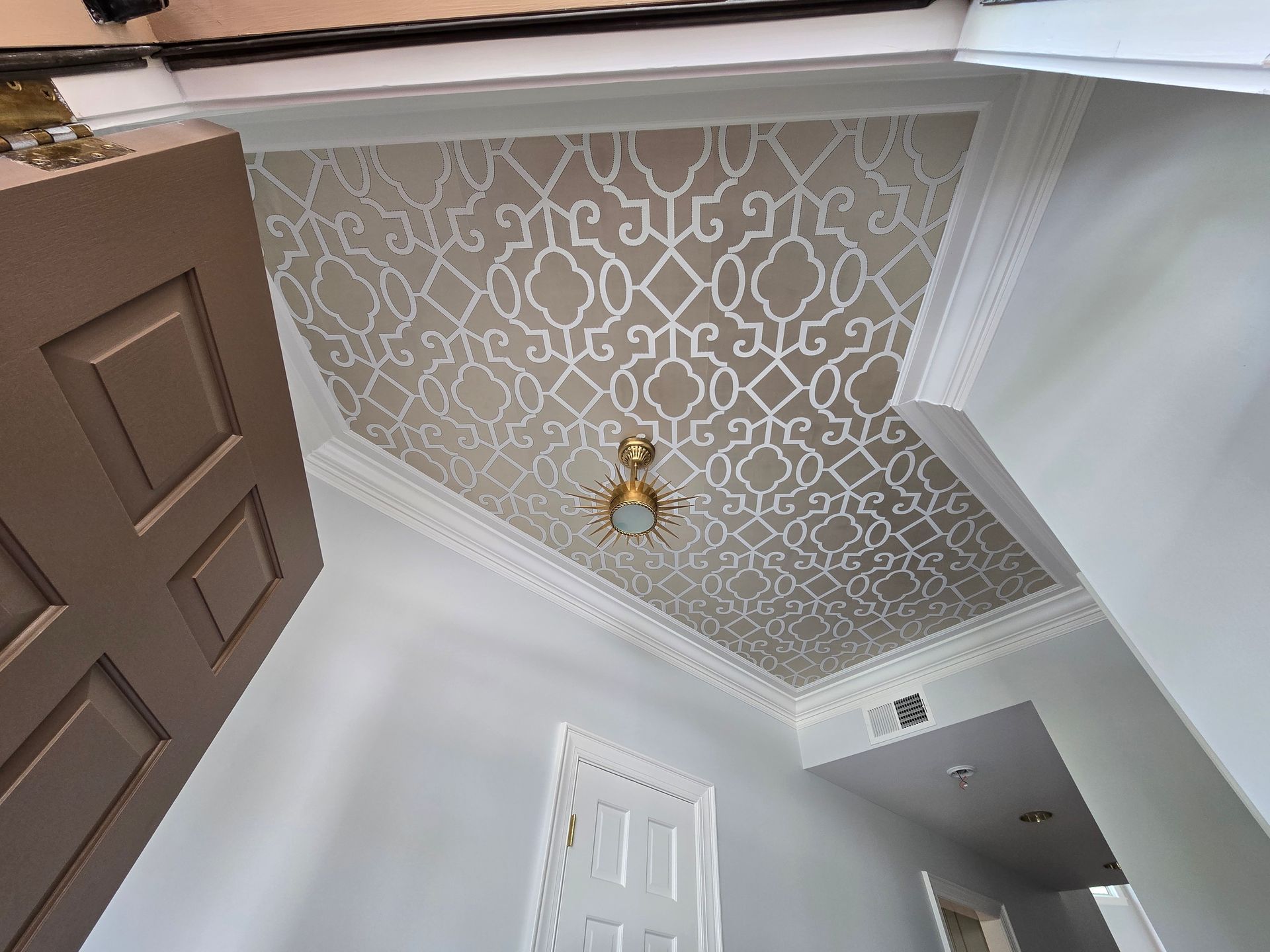 Low-angle view of a white hallway ceiling featuring a beige and white Moroccan-style geometric wallpaper pattern.