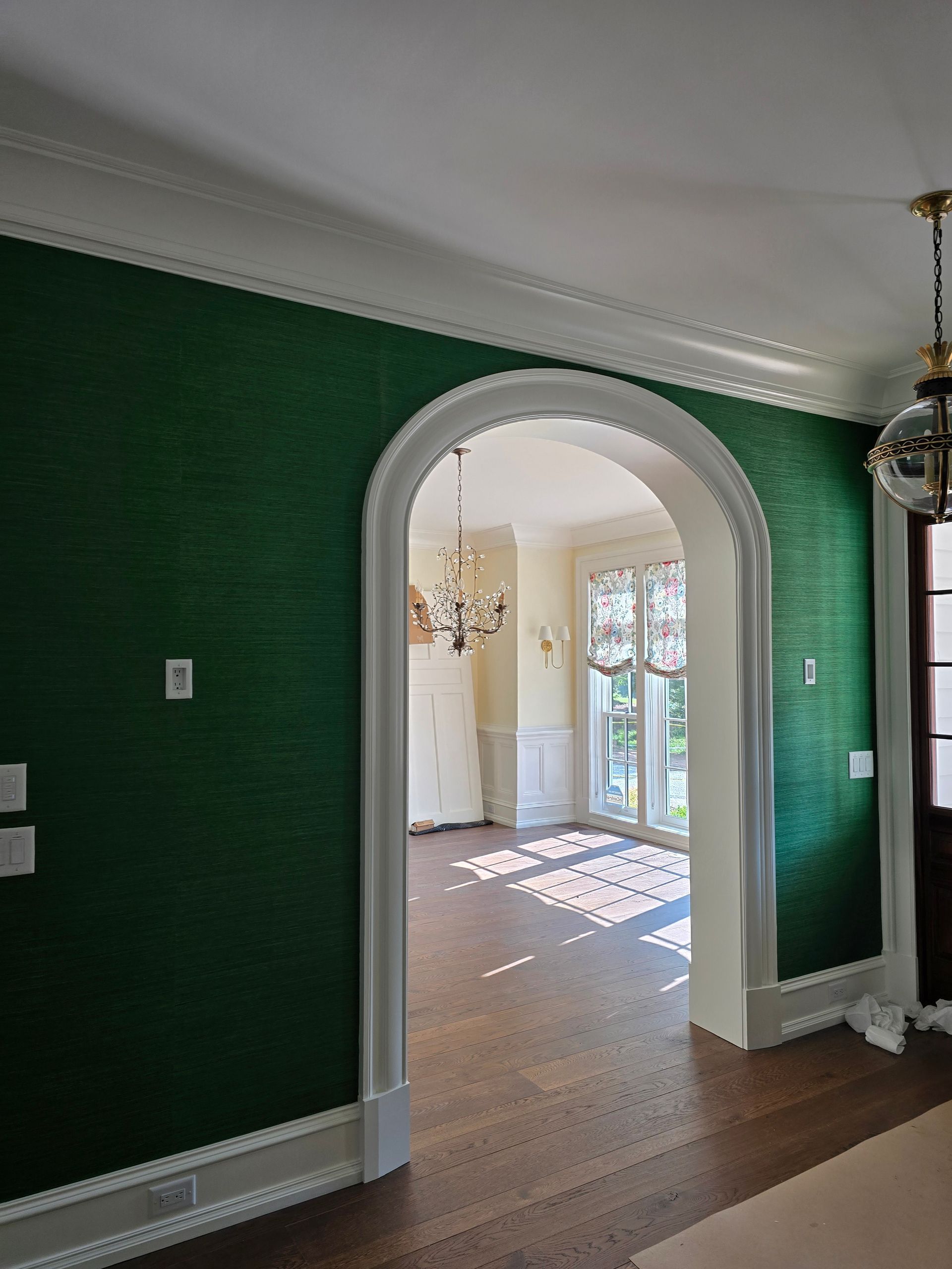 A dark green textured wall with a white arched doorway leading to a bright, sunlit room with hardwood floors.