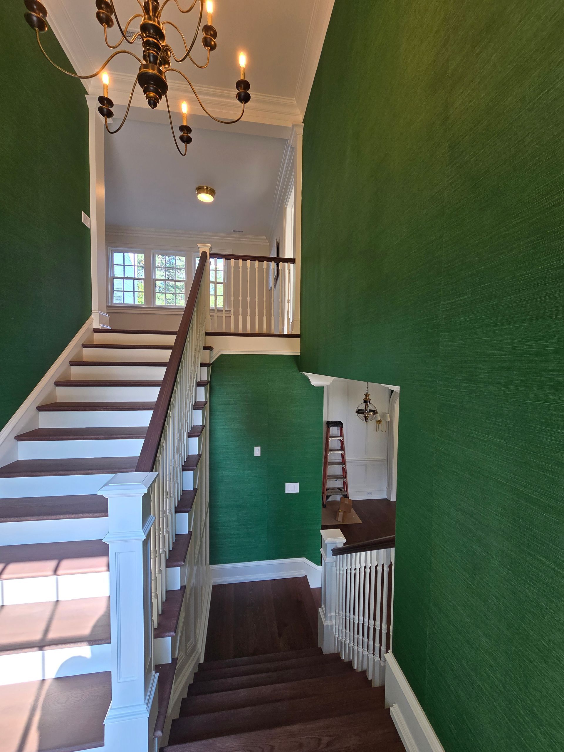 A foyer with dark green walls, a chandelier, and a white staircase leading both upward and to a lower landing.