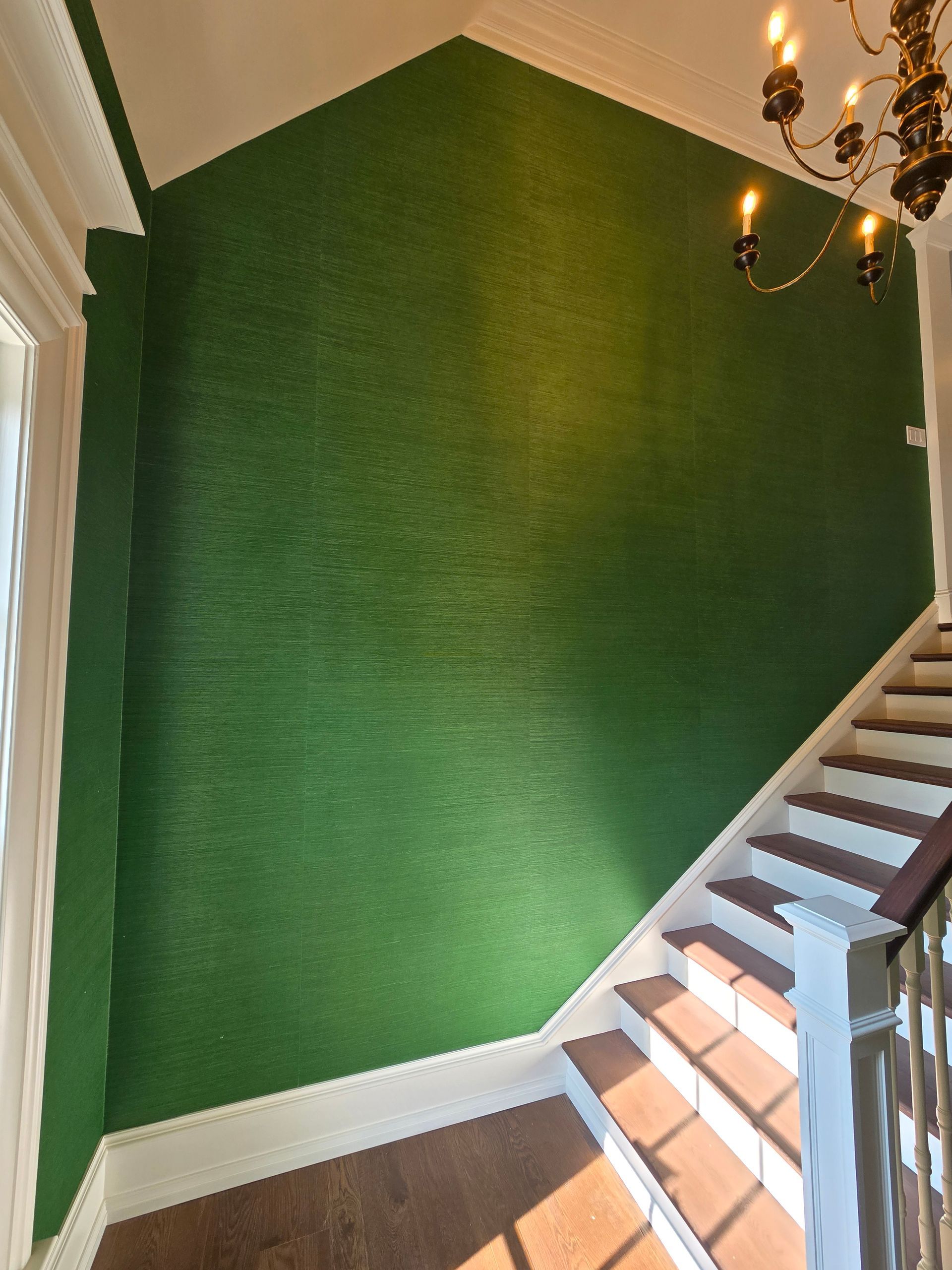 A tall, textured deep-green accent wall in a foyer, featuring a vaulted ceiling, wooden staircase, and chandelier.